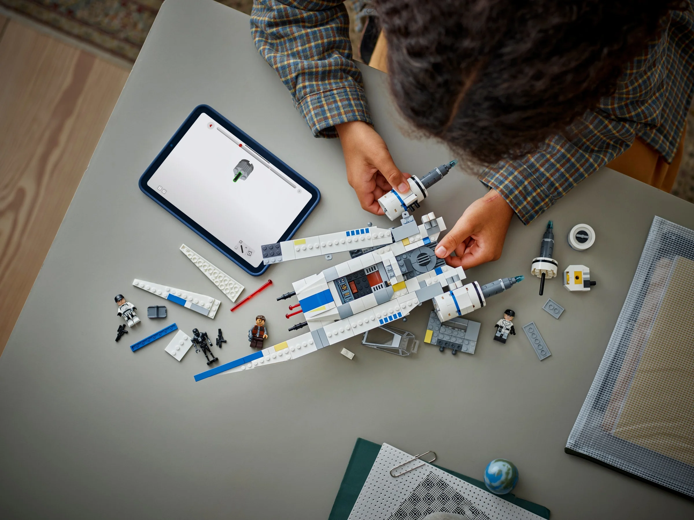 Copil asamblând U-wing Starfighter urmând instrucțiunile de pe tabletă. O imagine detaliată.