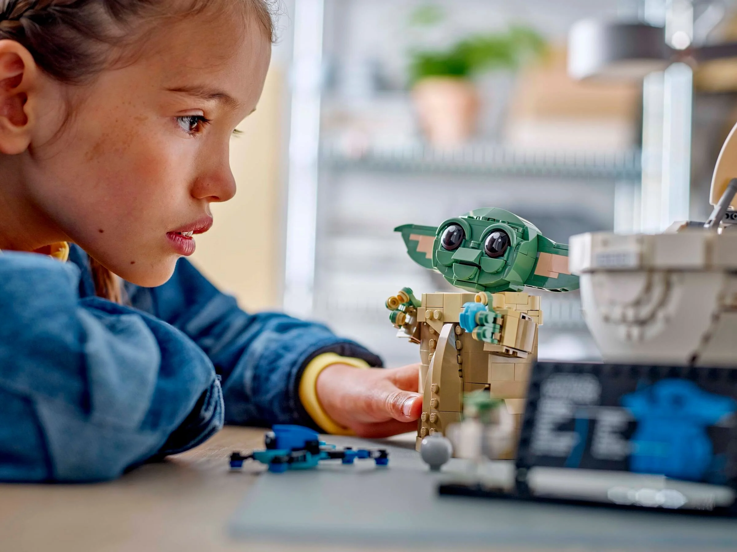 Copil admirând setul LEGO Grogu cu Hover Pram. Concentrare și bucurie, o experiență creativă.