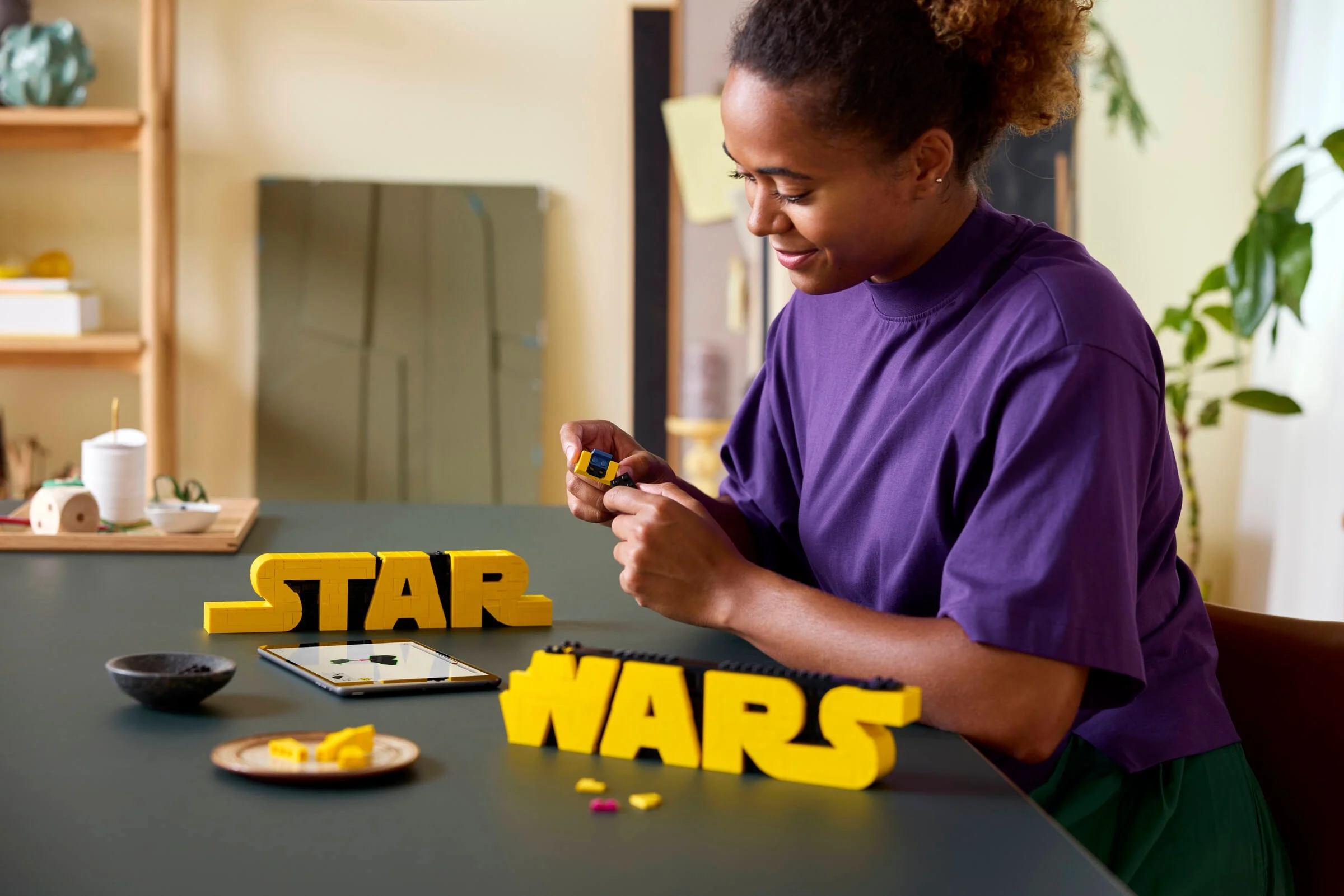 Femeie construind logo-ul Star Wars din cărămizi LEGO. Setul LEGO 75497 e în prim-plan.