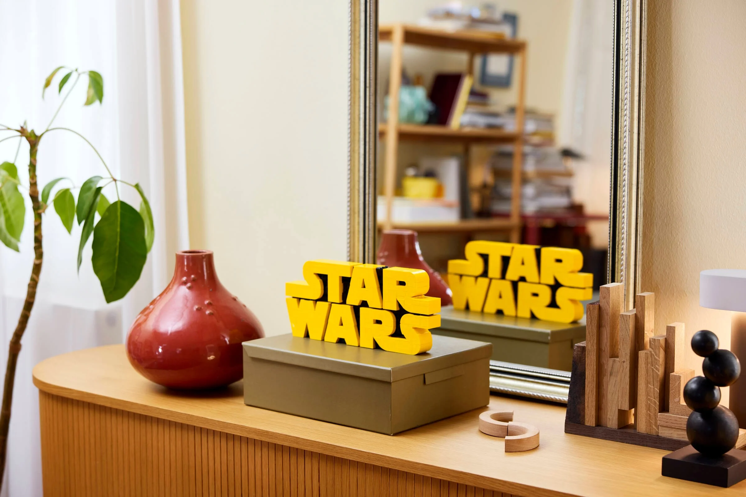 Sigla Star Wars construită din cărămizi LEGO, expusă pe o comodă elegantă. Decor viu.