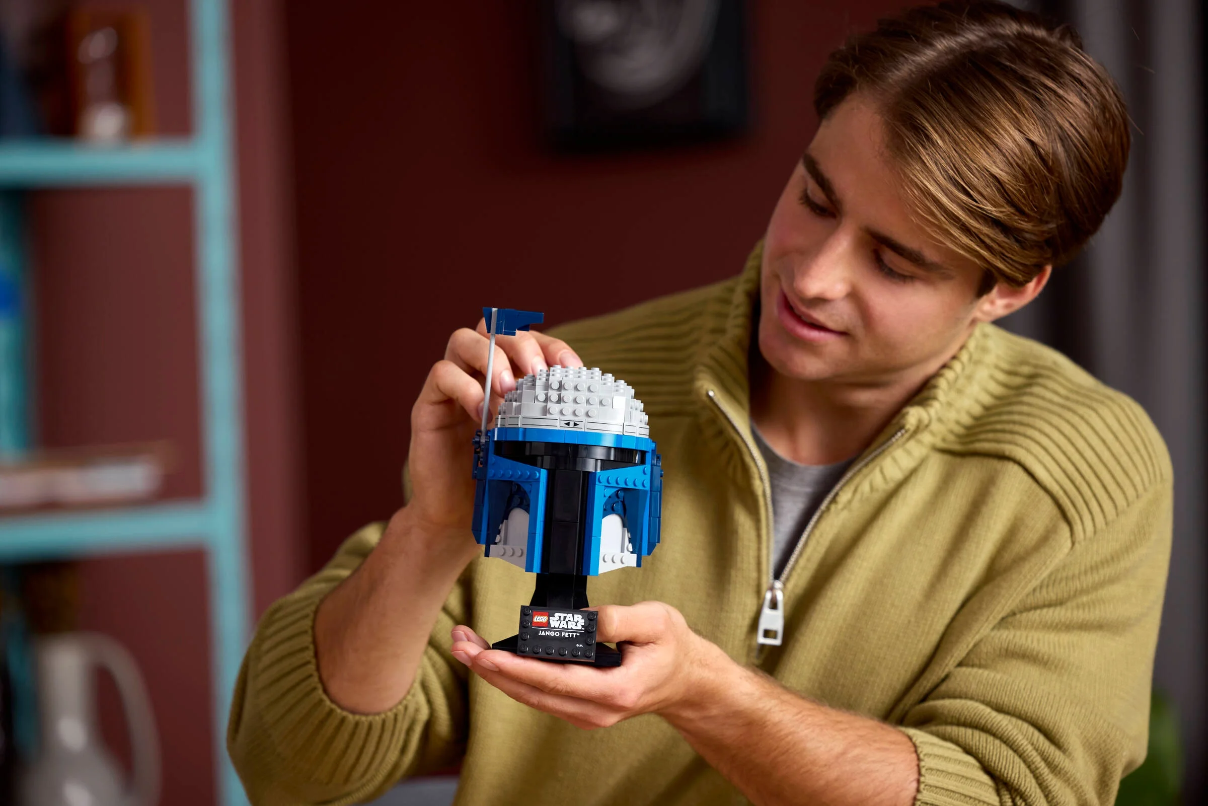 Bărbat admirând casca LEGO Jango Fett, detaliată și colorată, pe suportul său.