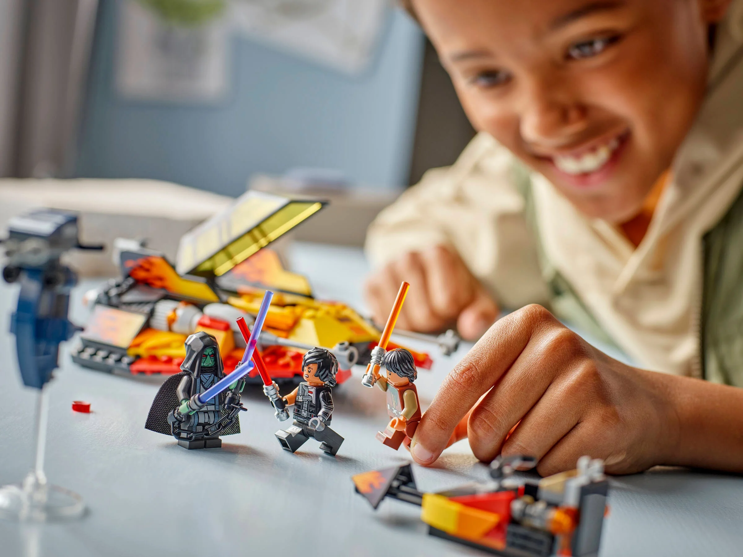 Un copil se joacă cu minifigurinele LEGO Star Wars, inclusiv Snowspeeder-ul. Zâmbește cu entuziasm.