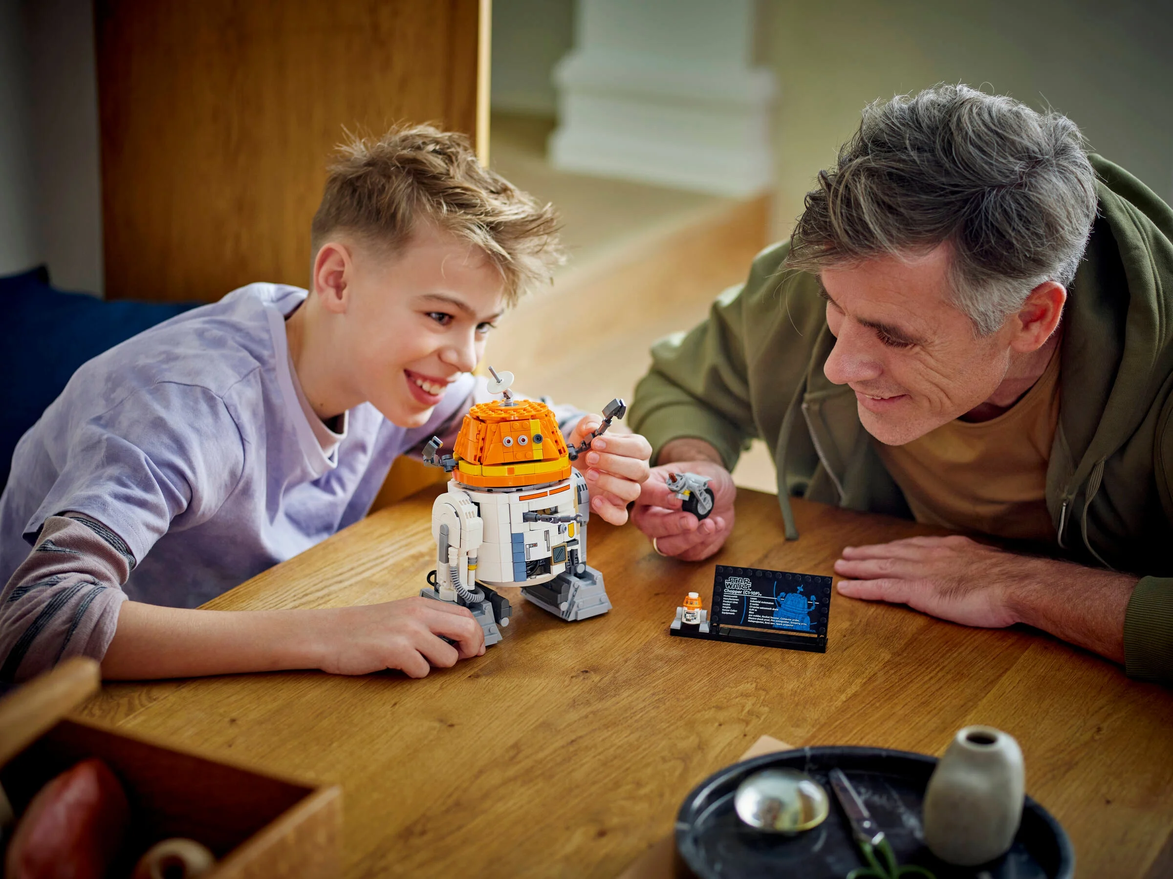 Un tată și fiu construiesc modelul LEGO Chopper (C1-10P) împreună, zâmbitori.