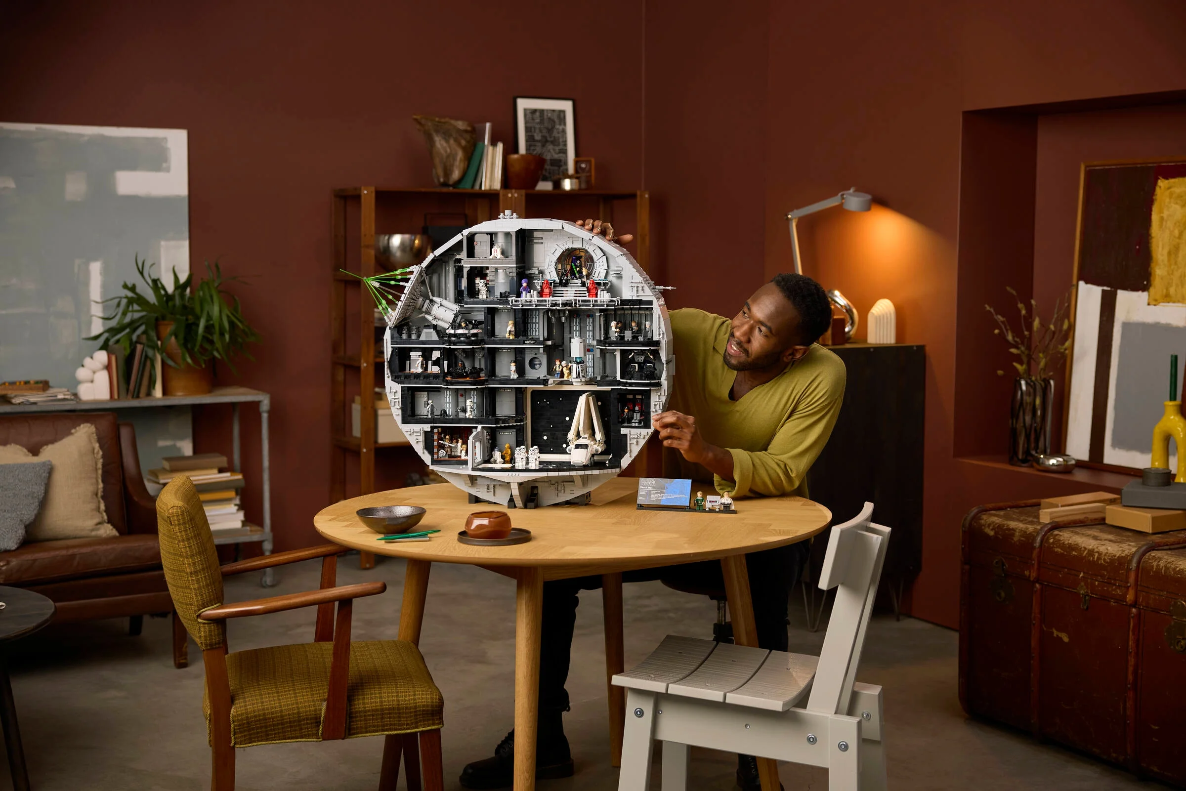 Un adult ține modelul Death Star, arătând detaliile interioare. O scenă relaxată, de prezentare.