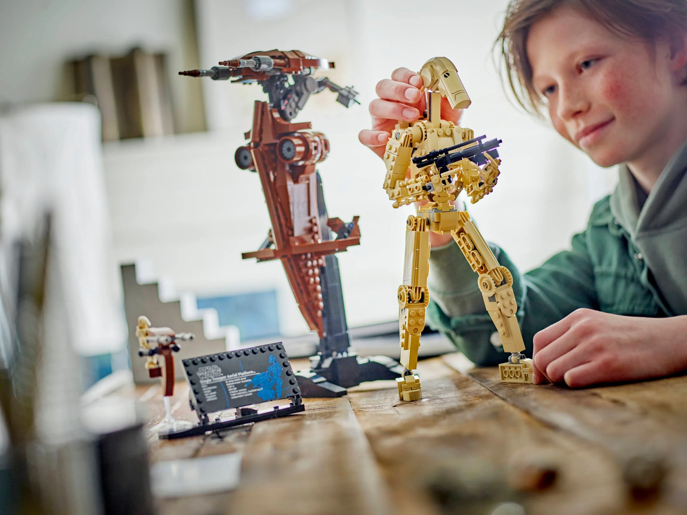Un copil construiește droidul de luptă LEGO Star Wars cu STAP pe o masă de lemn.