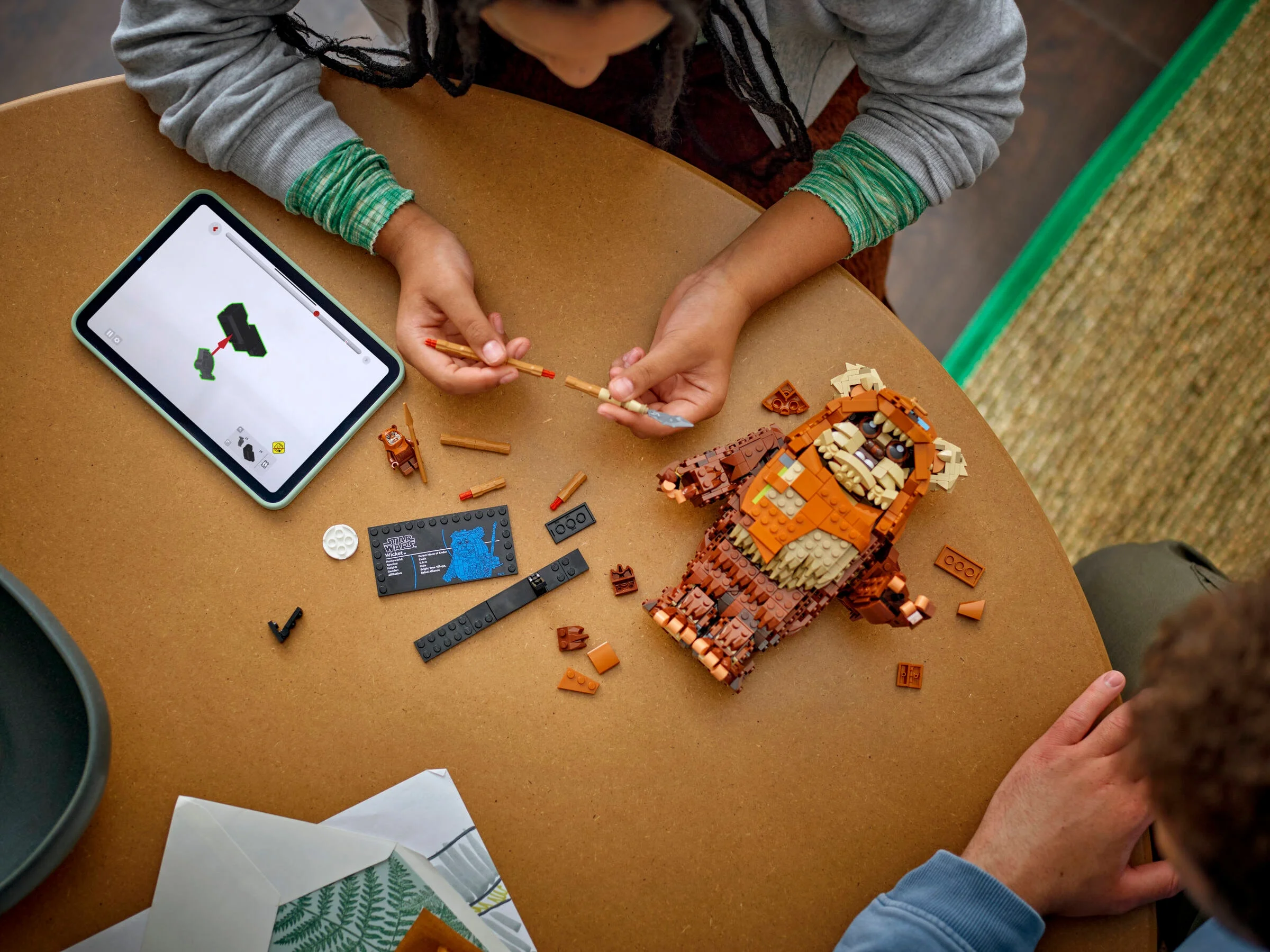 Imagine de sus cu cineva care construiește LEGO Wicket Ewok cu instrucțiuni pe tabletă.