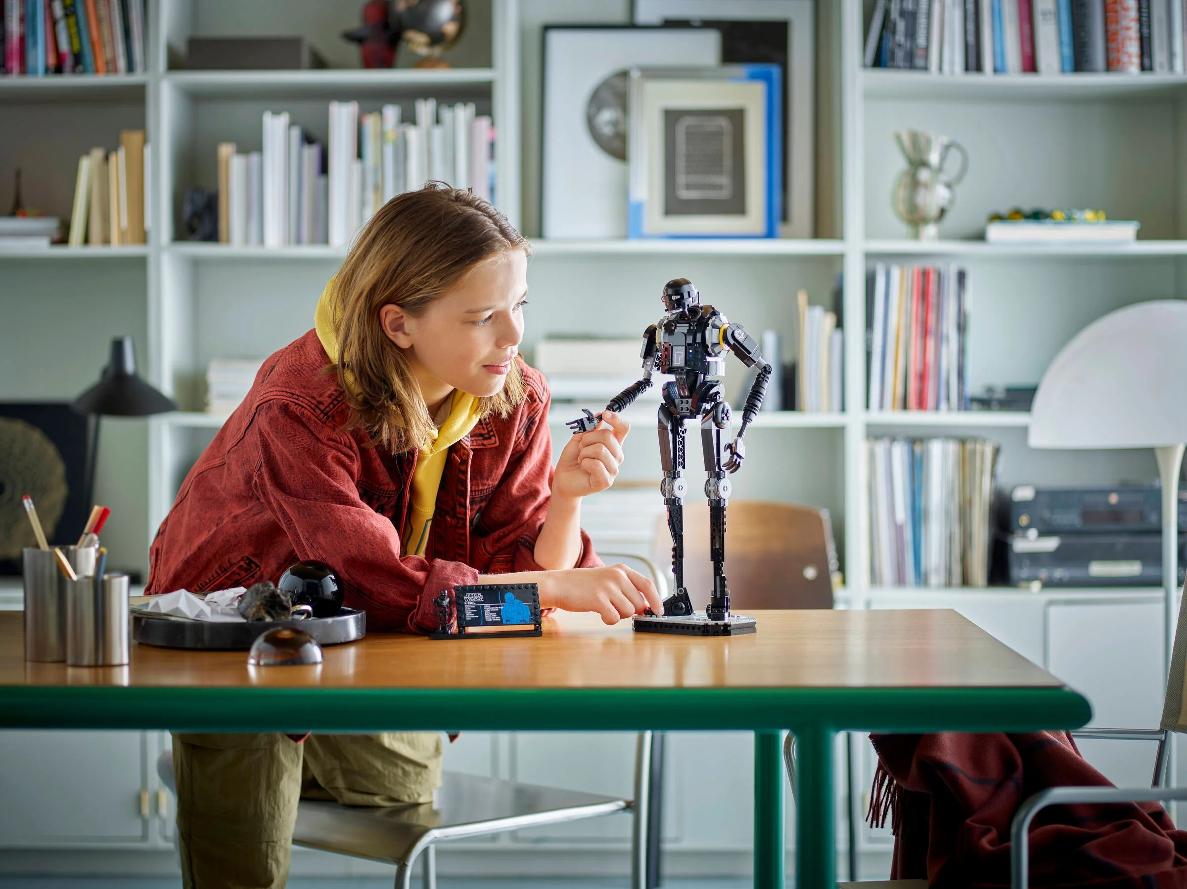 O fată admiră figurina LEGO K-2SO construită pe o masă.