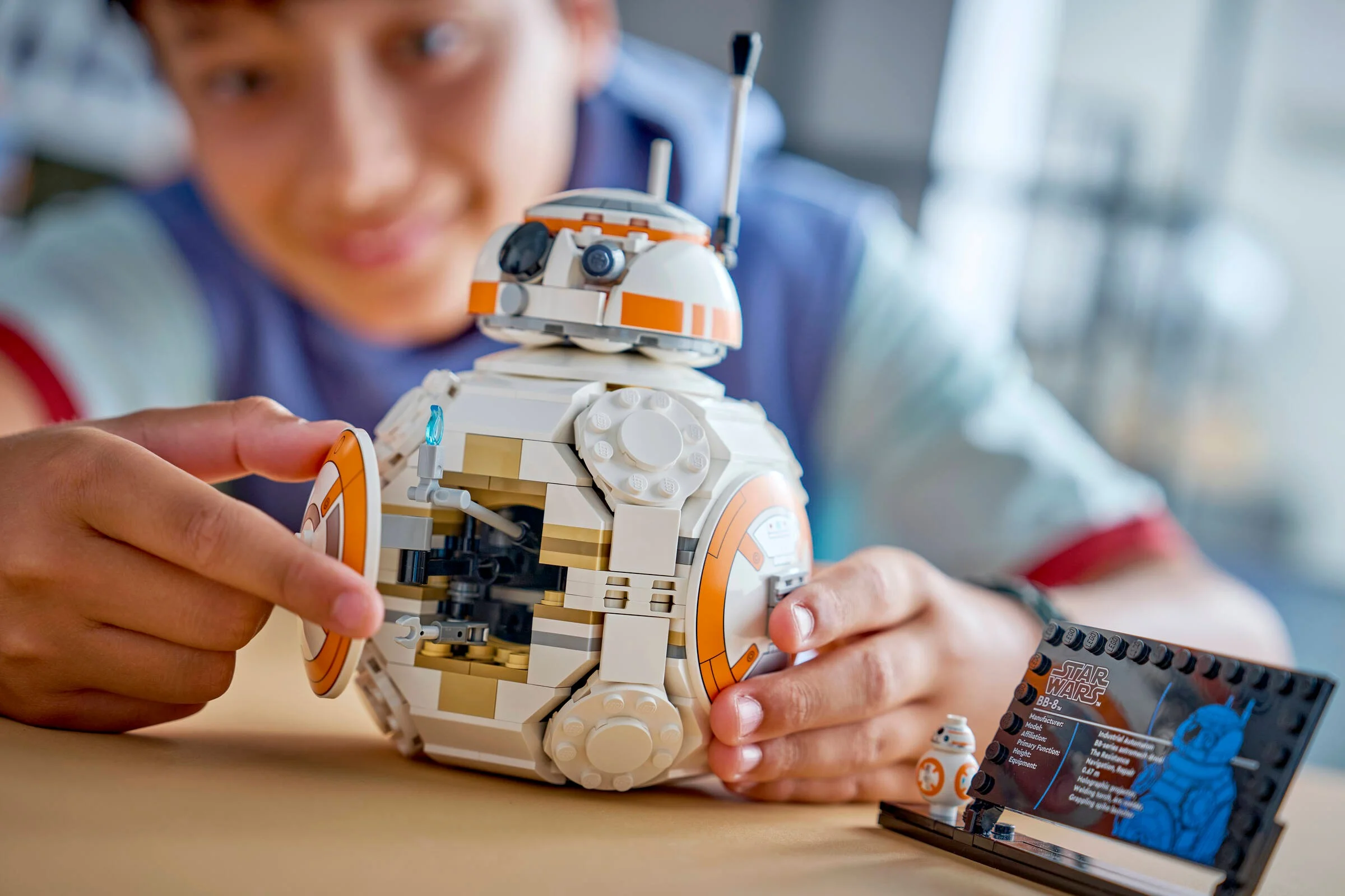 Copil interacționând cu BB-8 LEGO. Machetă detaliată, inclusiv placa informativă. O imagine atractivă.
