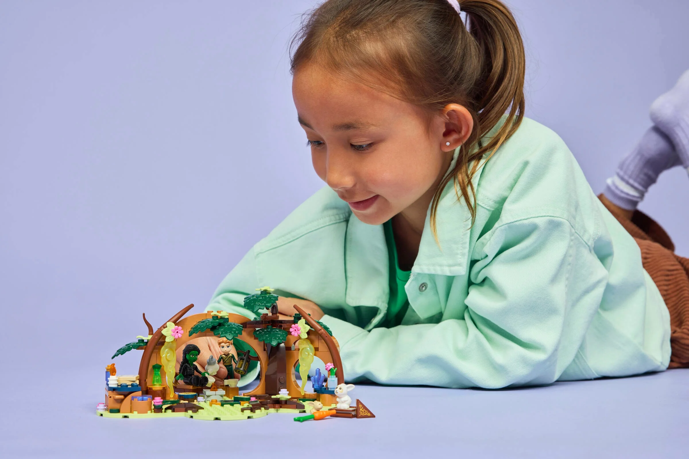 Fată se joacă cu setul LEGO 75687, „Elphaba's Retreat”. Detalii ale modelului și minifigurinele vizibile.