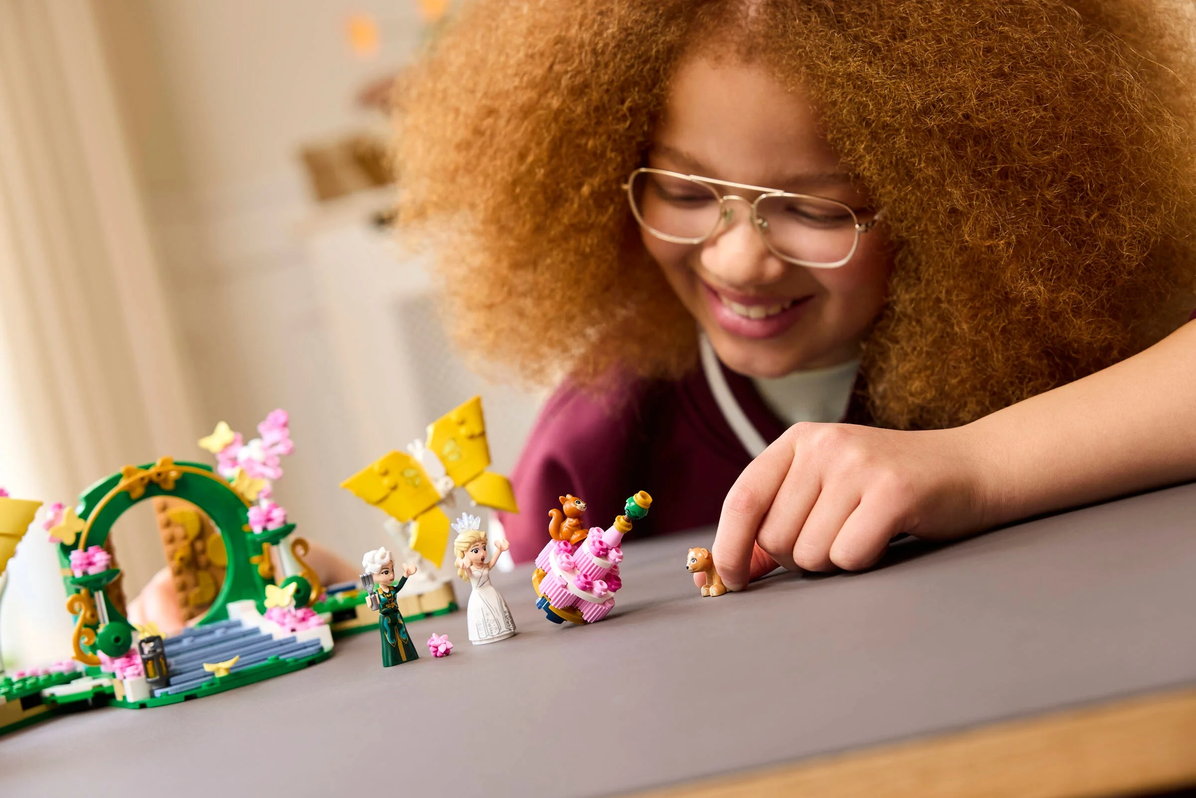 Copil zâmbitor se joacă cu setul LEGO Nunta Glindei, aranjând figurine și elemente decorative.