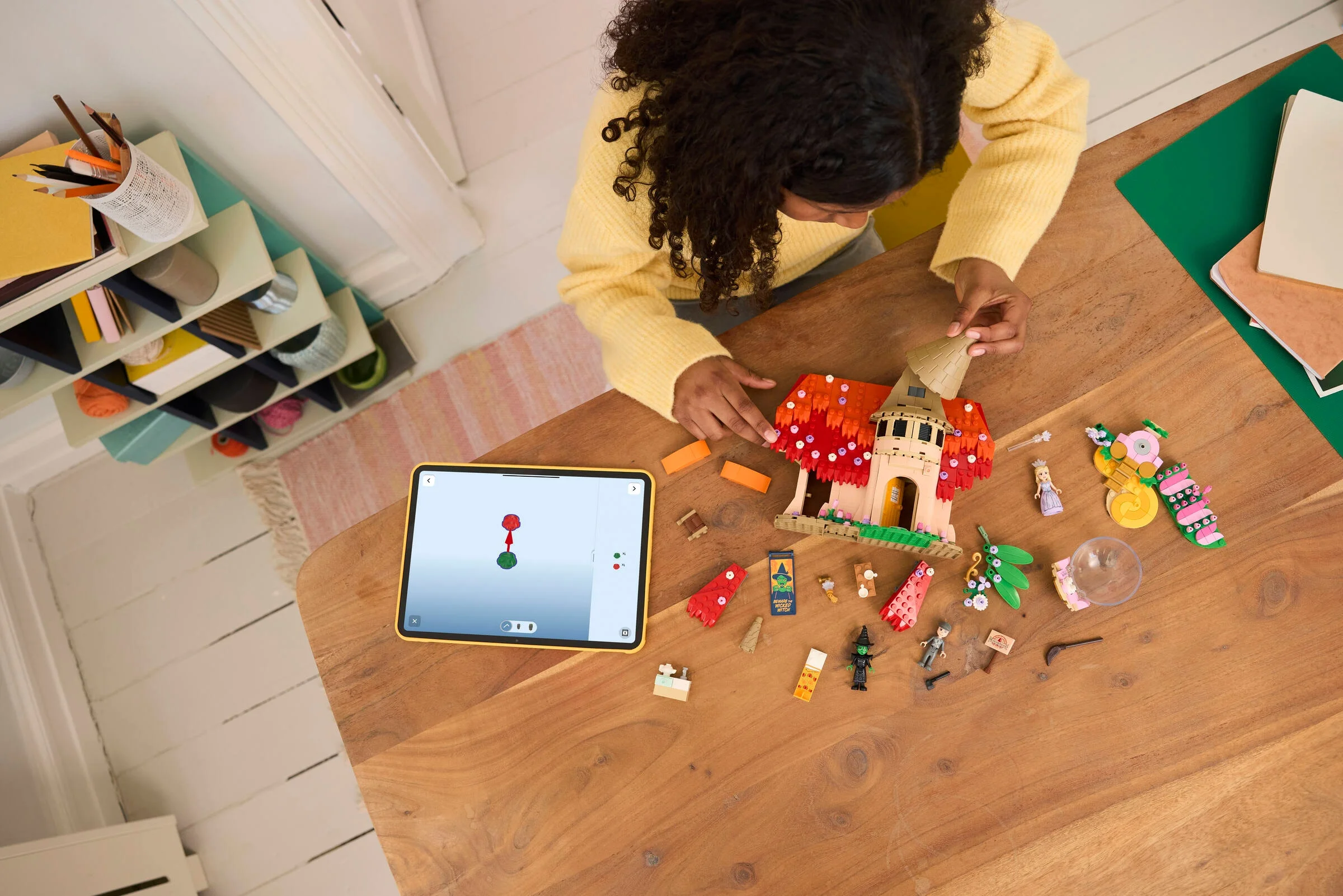O fată construiește căsuța Munchkinland din LEGO, urmărind instrucțiunile pe tabletă.