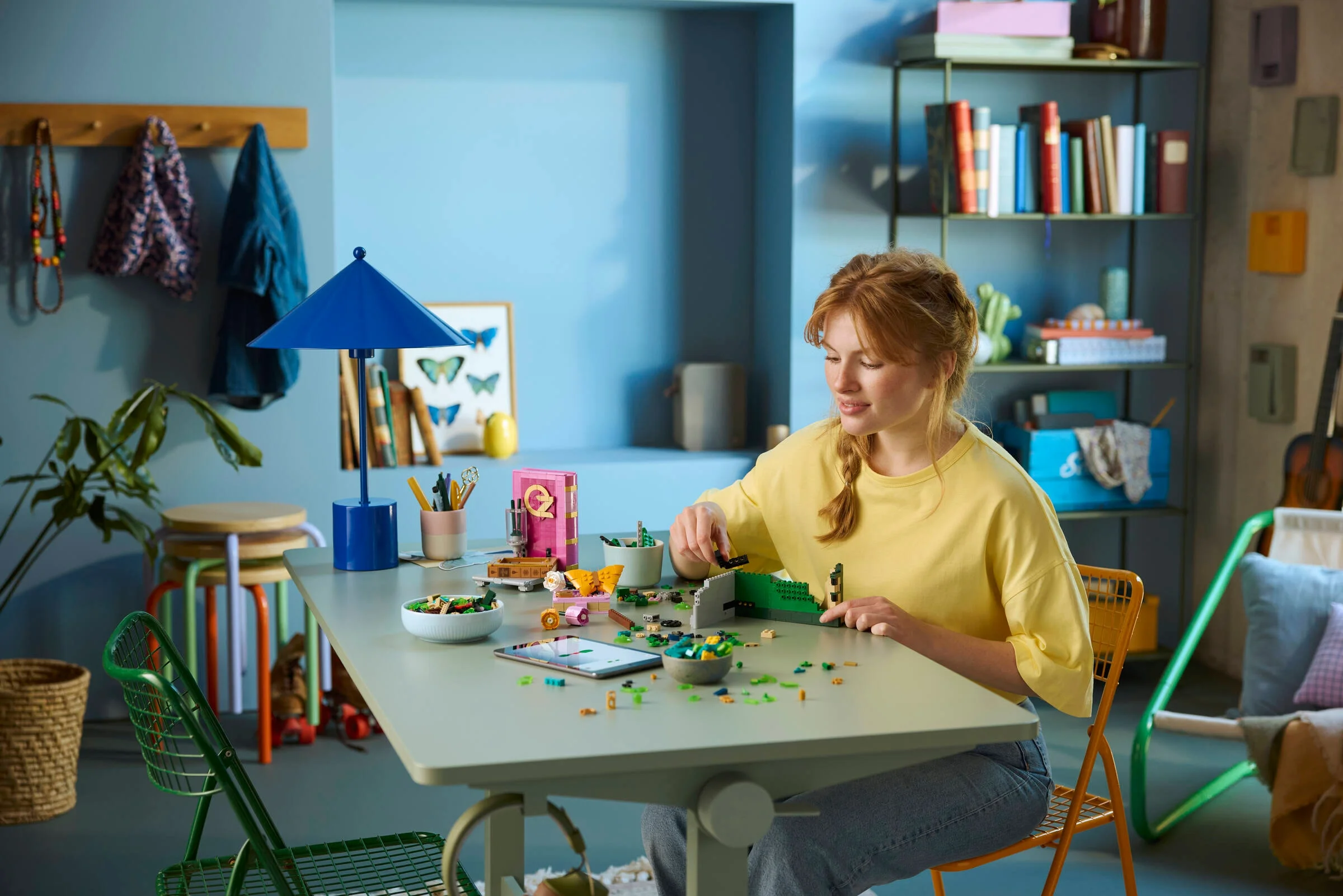 Femeie construind setul LEGO Glinda & Elphaba Bookends. Piese împrăștiate pe masă, focus pe construcție.