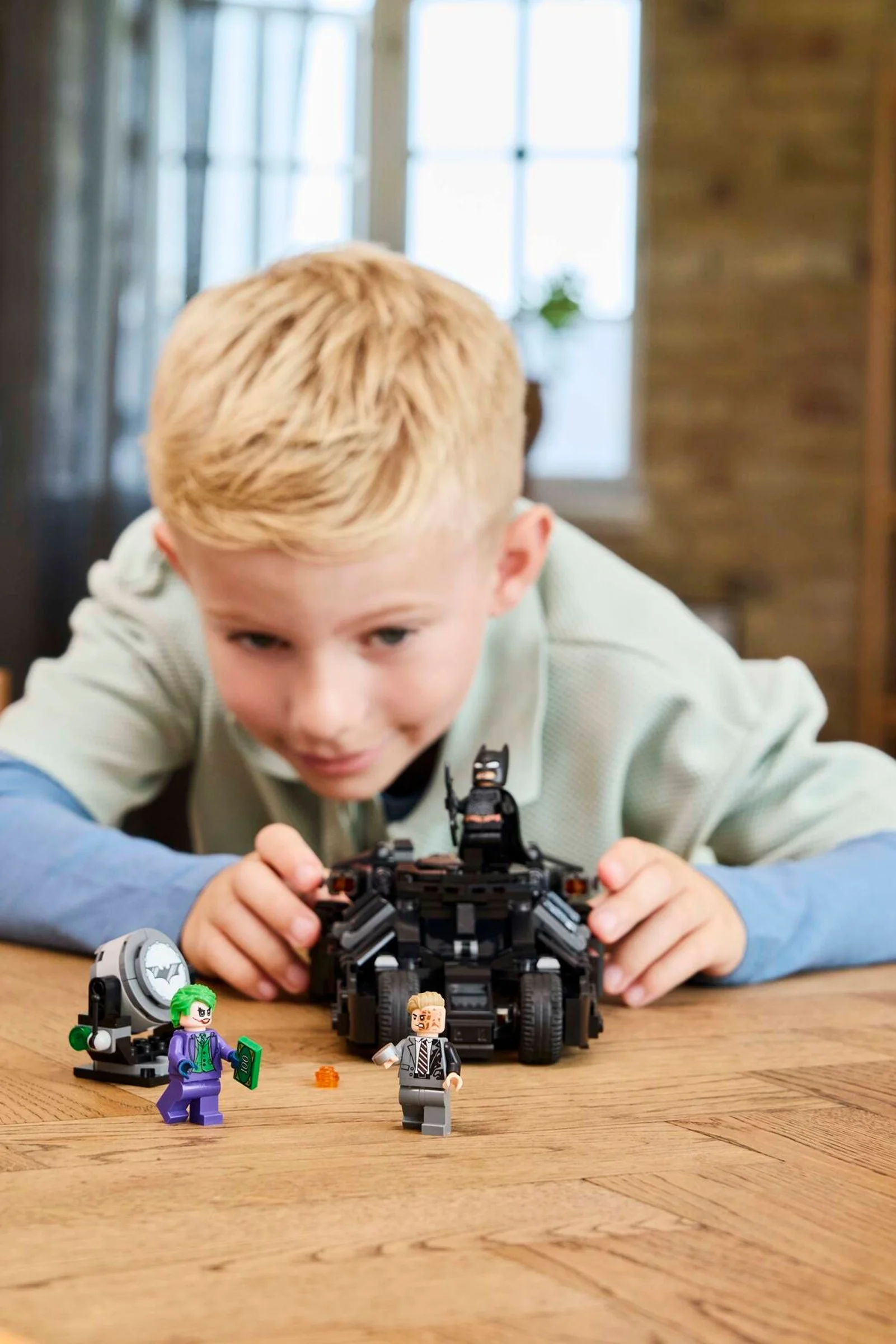 Un copil se joacă cu setul LEGO Batman Tumbler împotriva lui Two-Face și Joker.