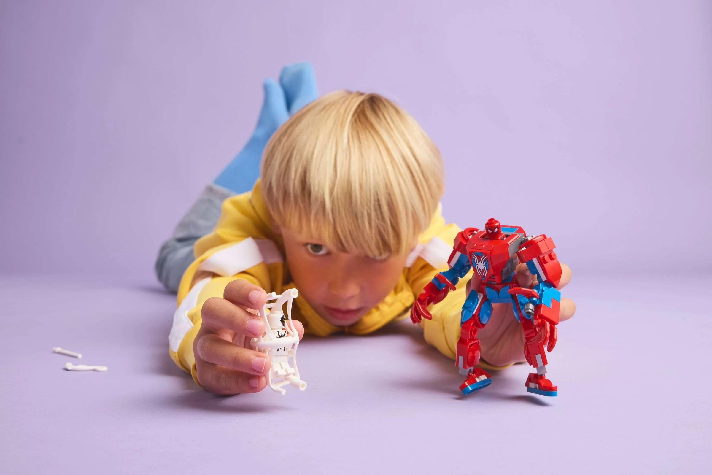 Băiat se joacă cu roboții LEGO Spider-Man și Anti-Venom pe un fundal violet.