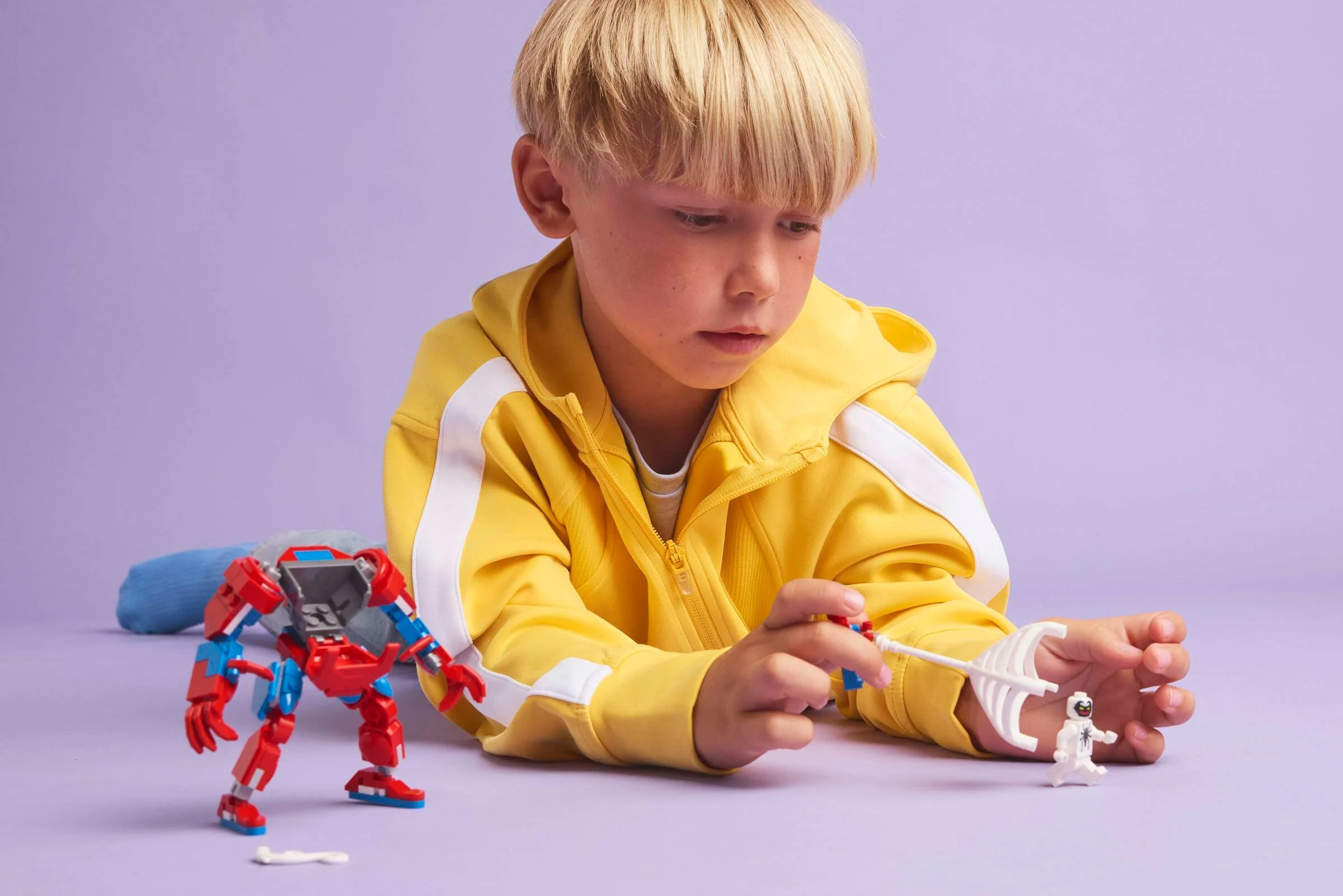 Copil se joacă cu setul LEGO Spider-Man Mech vs. Anti-Venom, arătând figurinele și mech-ul.