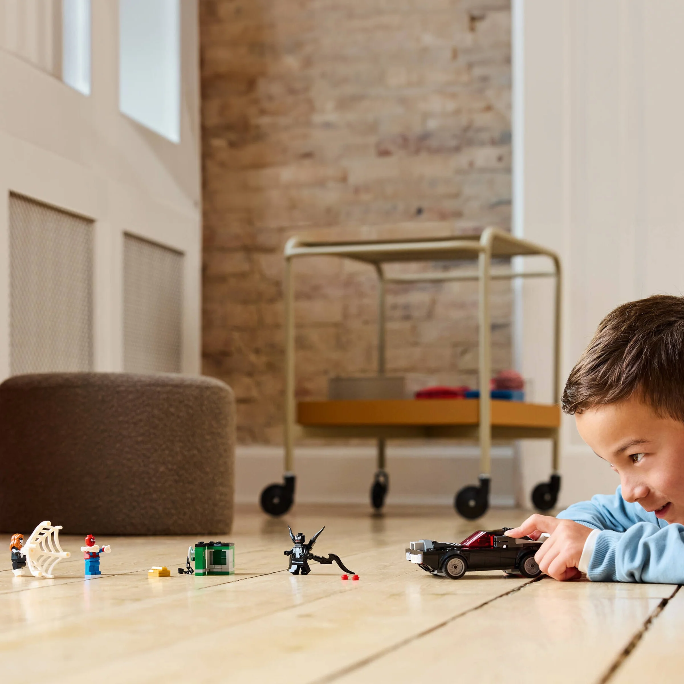Un băiat se joacă cu mașina și minifigurinele LEGO Spider-Man vs. Venom pe podea.