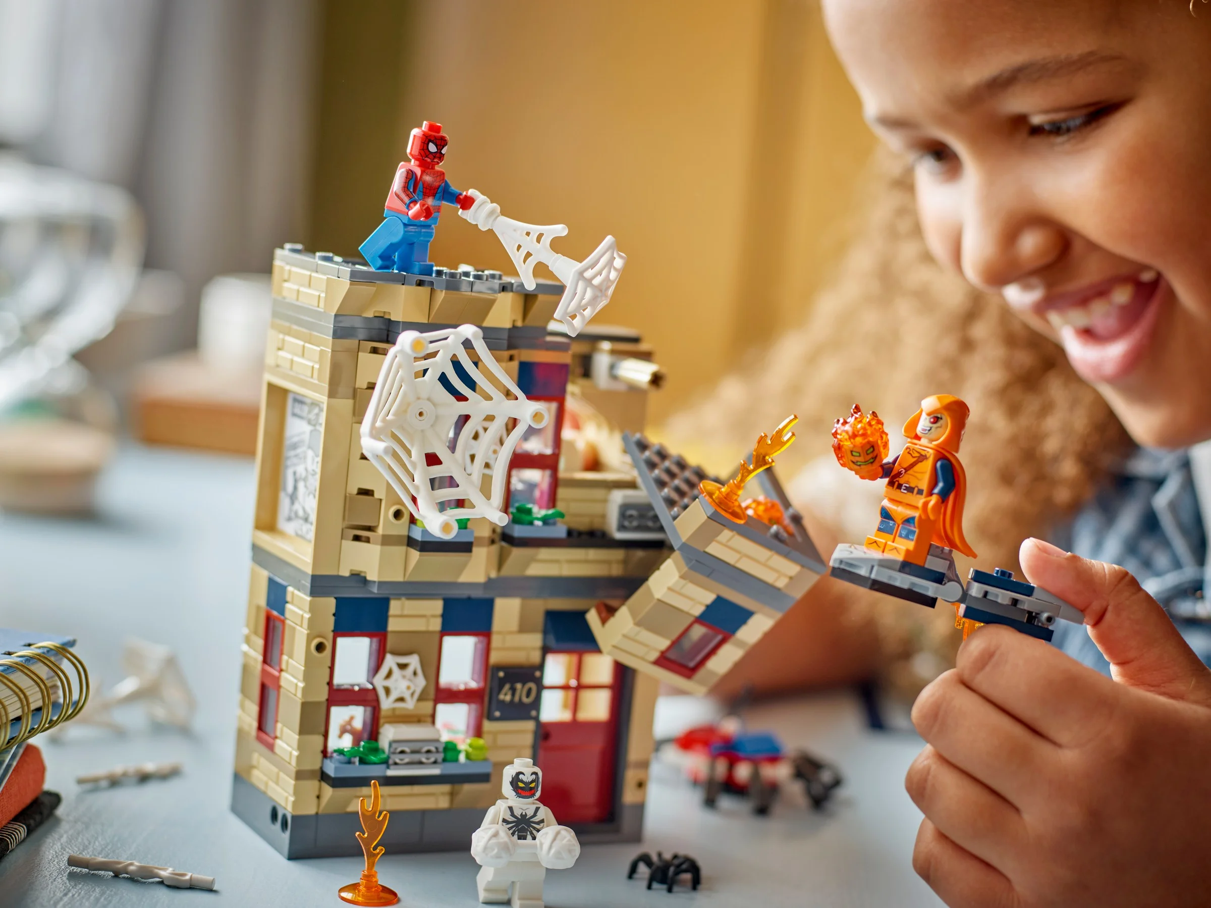 Fetiță zâmbind, se joacă cu setul LEGO 76317, prezentând minifigurine și caracteristici ale apartamentului.