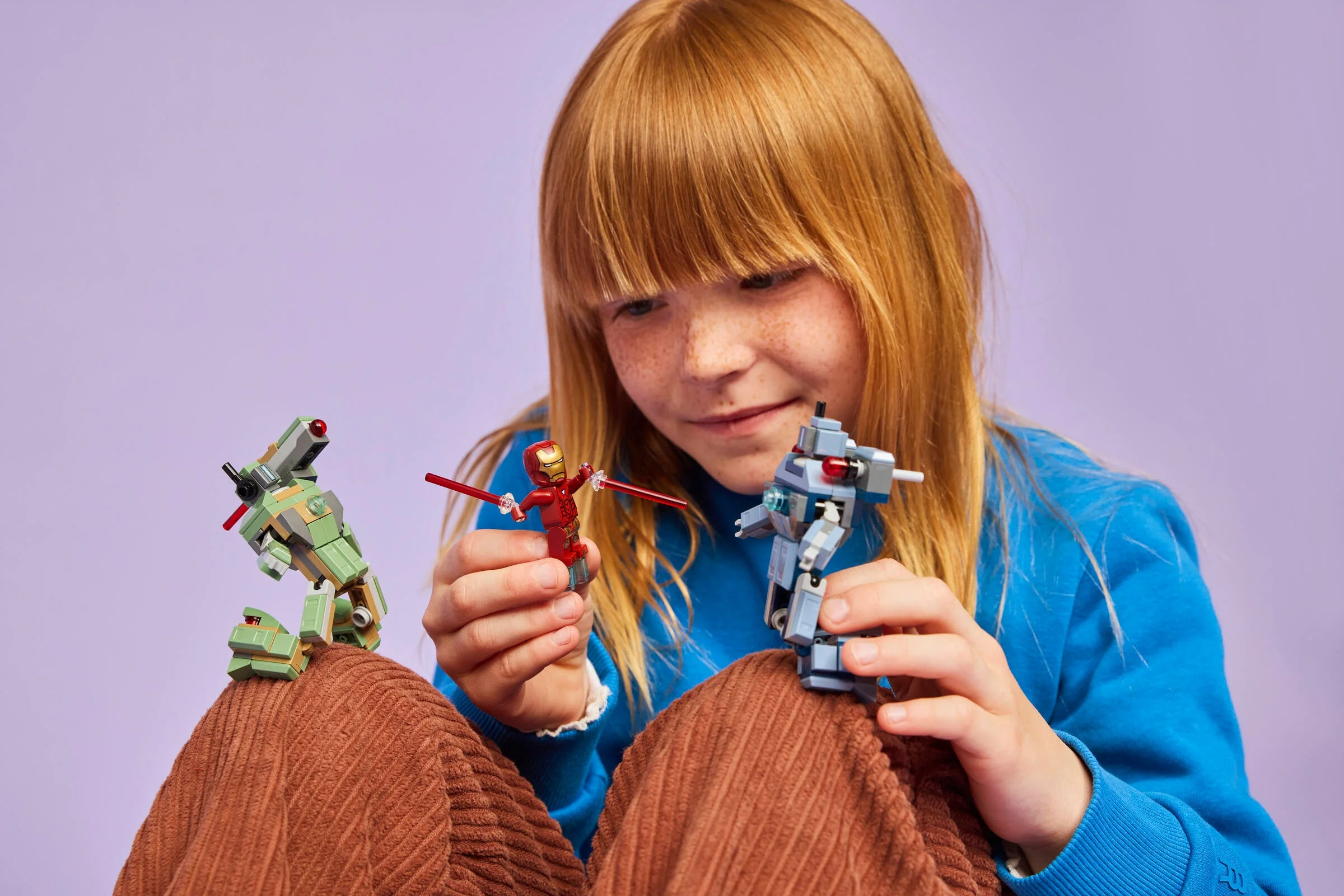 O fetiță se joacă cu minifigurinele LEGO Iron Man și Drone Hammer.