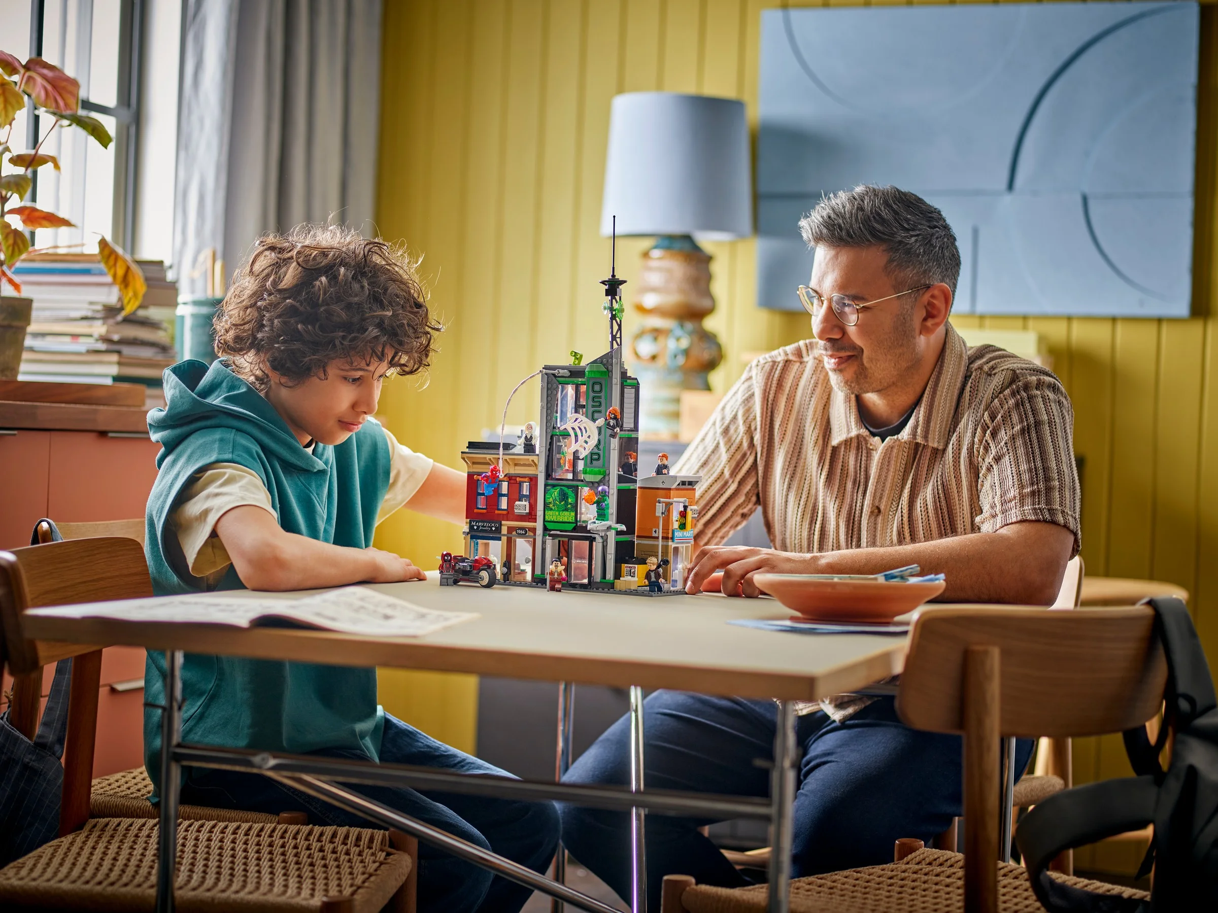 Copil și adult construind setul LEGO Spider-Man vs. Oscorp, râzând.