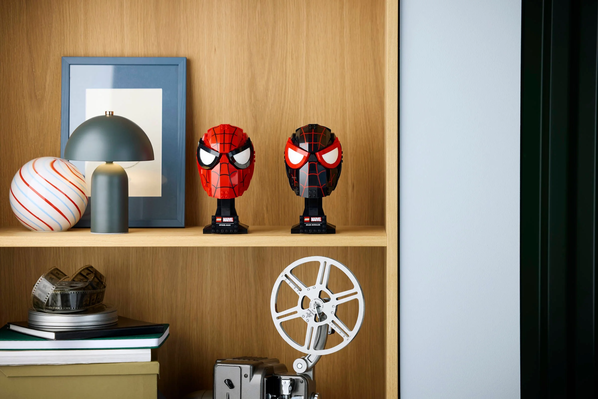Măștile LEGO Spider-Man și Miles Morales expuse pe un raft, într-un decor stilat.
