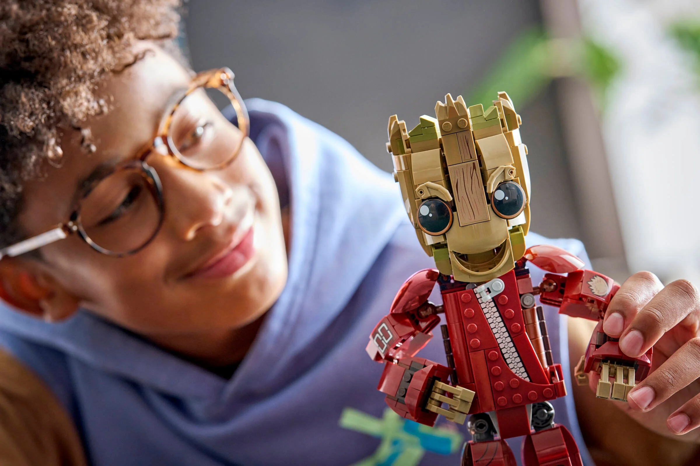 Copil zâmbitor admirând figurina LEGO Groot în costumul Ravager. O jucărie atractivă pentru fani.