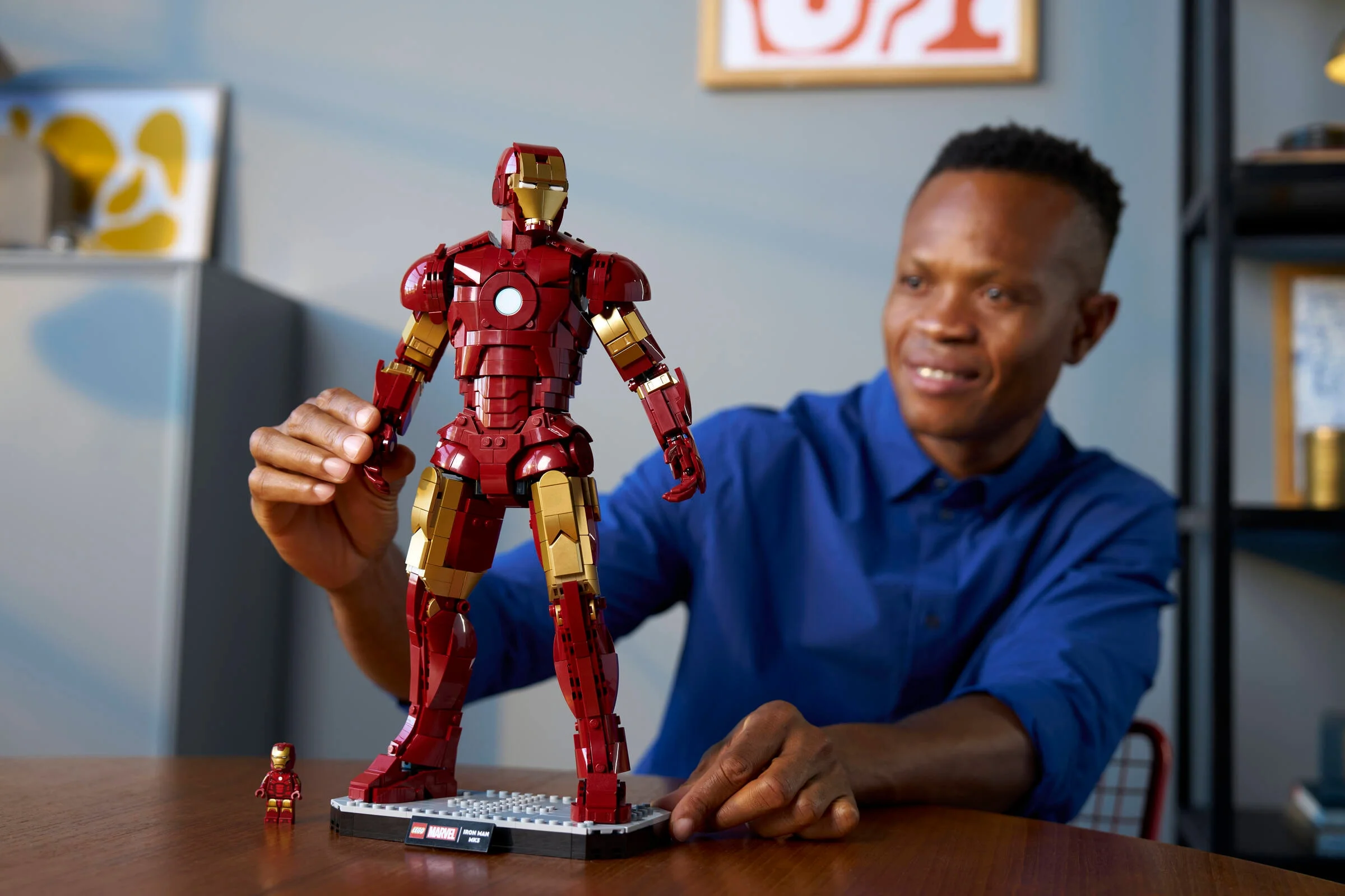 Bărbat admirând statuia Iron Man Mark 3 LEGO, cu o minifigurină lângă bază.