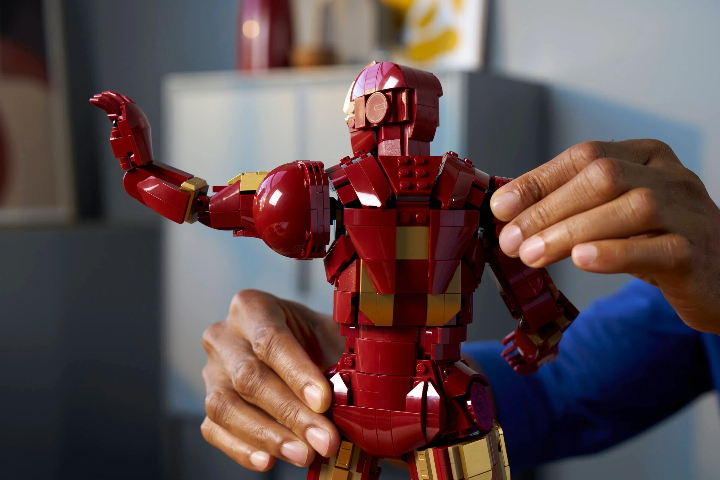 Mână umană ajustează poziția unui Iron Man Mark 3 din LEGO. Detaliu construcție și design.