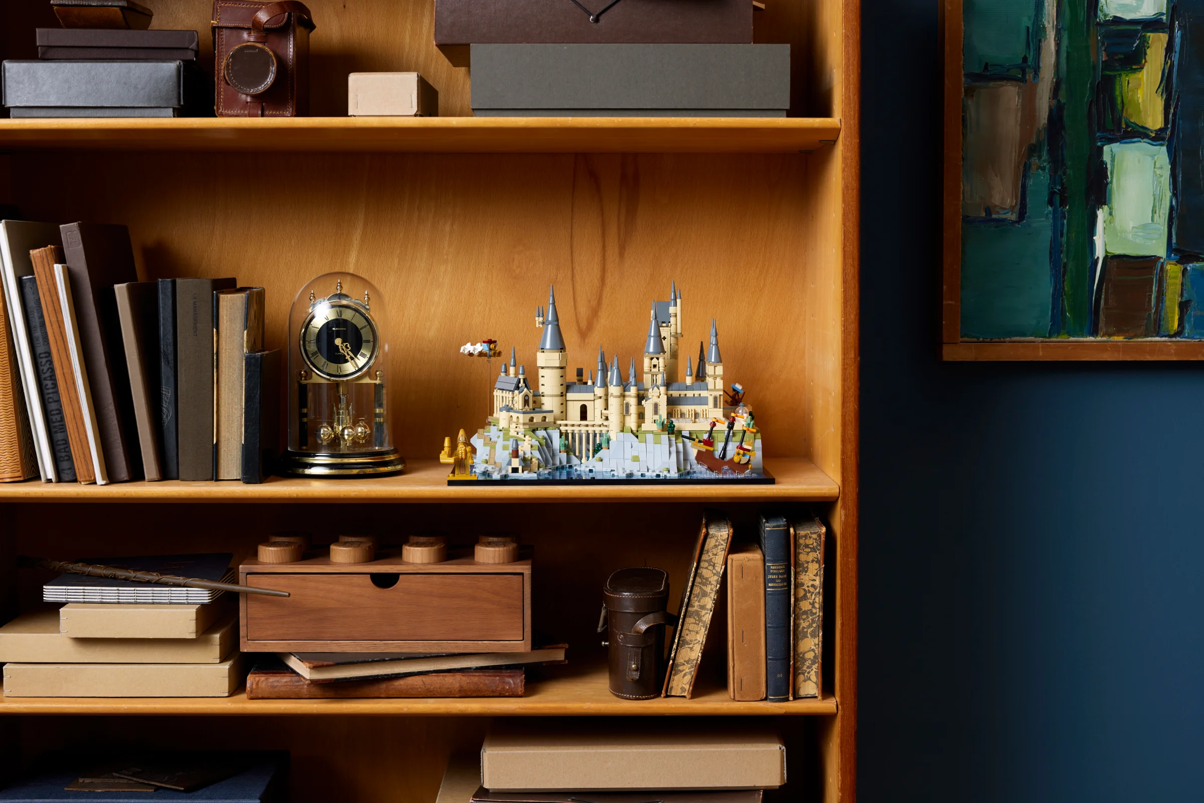 Hogwarts și terenurile sale LEGO, expuse pe un raft de bibliotecă. Model detaliat și atractiv.