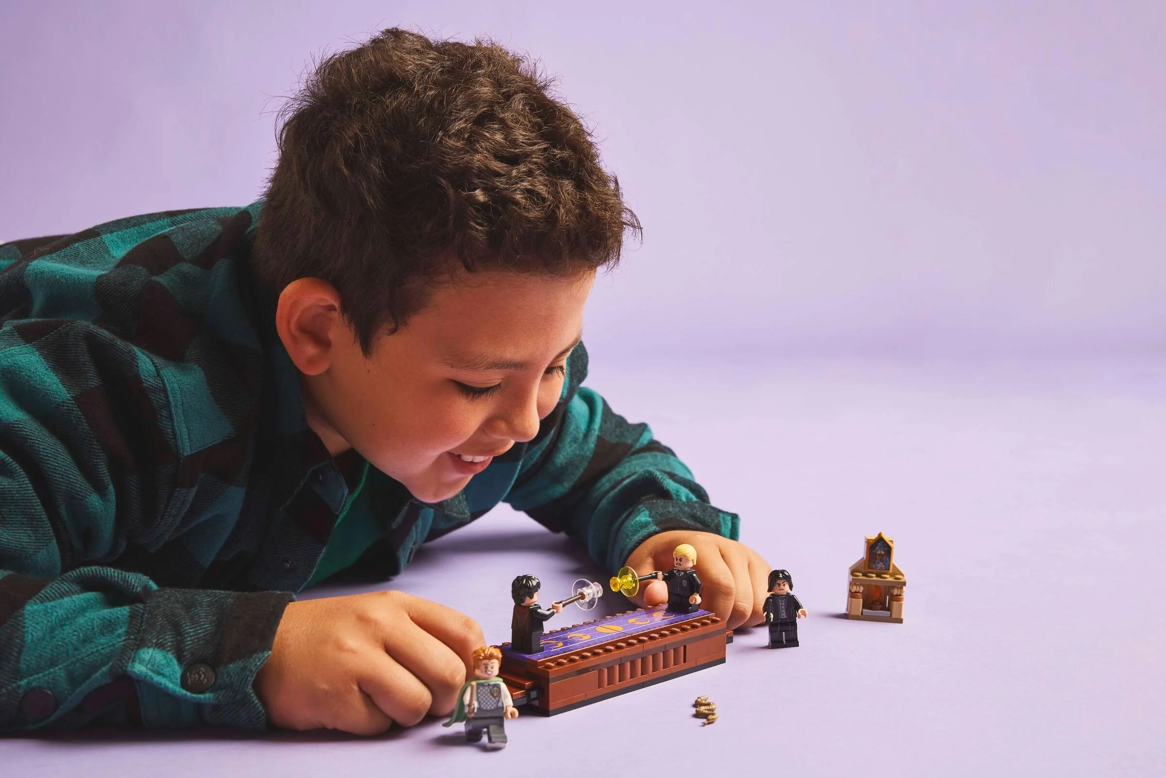 Băiat se joacă cu setul LEGO Dueling Club, zâmbind. Acțiunea se petrece pe un fundal mov.
