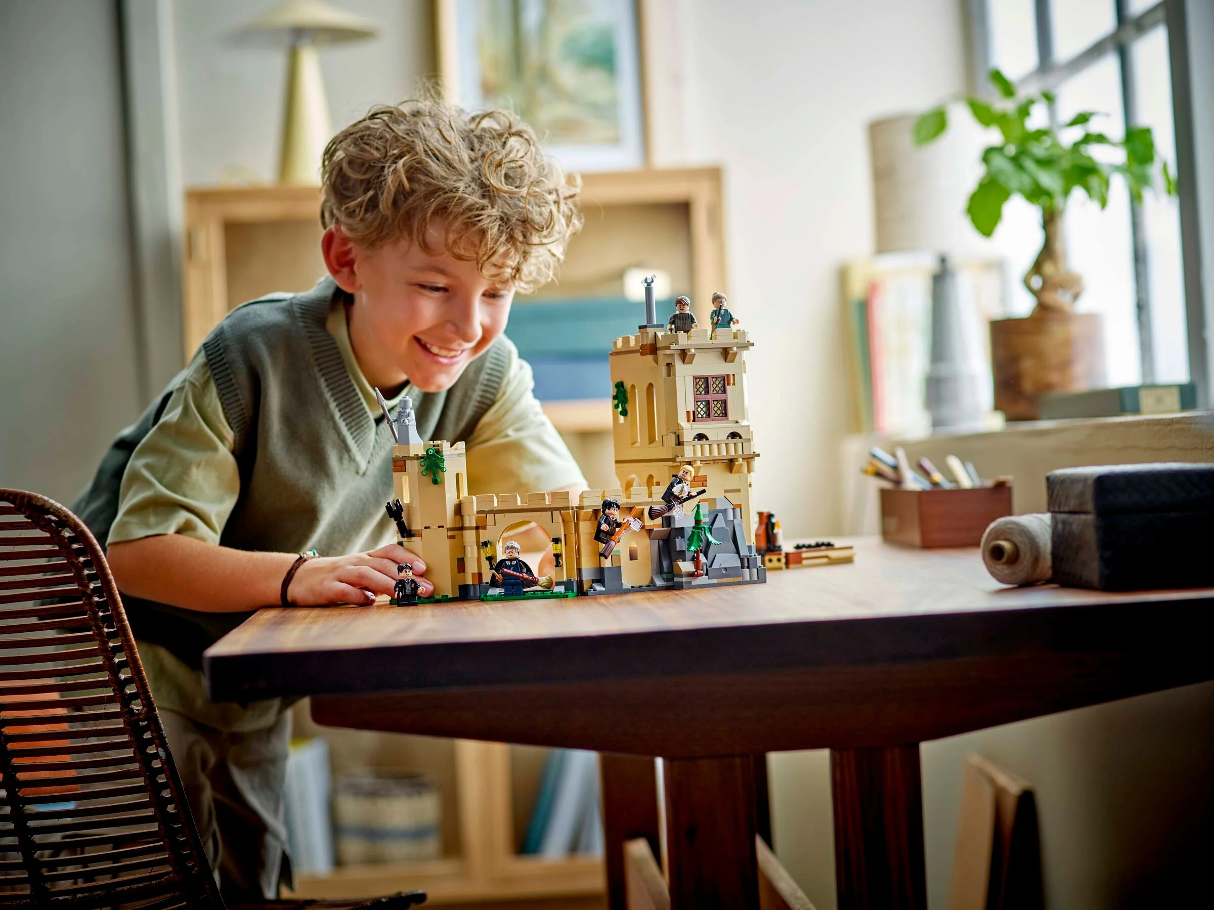Un băiat zâmbind se joacă cu setul LEGO Hogwarts: Lecții de Zbor pe o masă.
