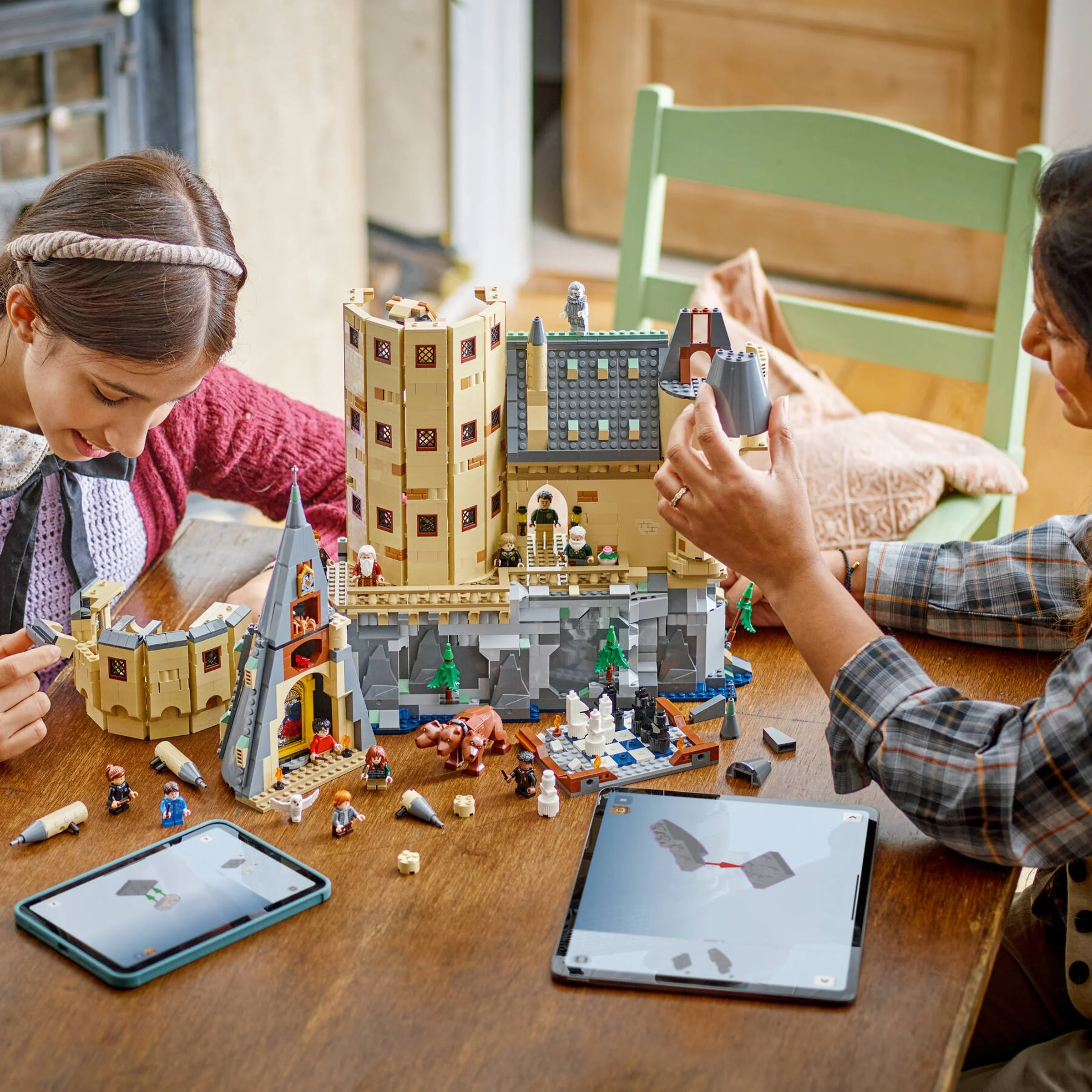 Două persoane asamblează setul LEGO Hogwarts Castle. Modelul, minifigurinele și tabletele cu instrucțiuni sunt vizibile.