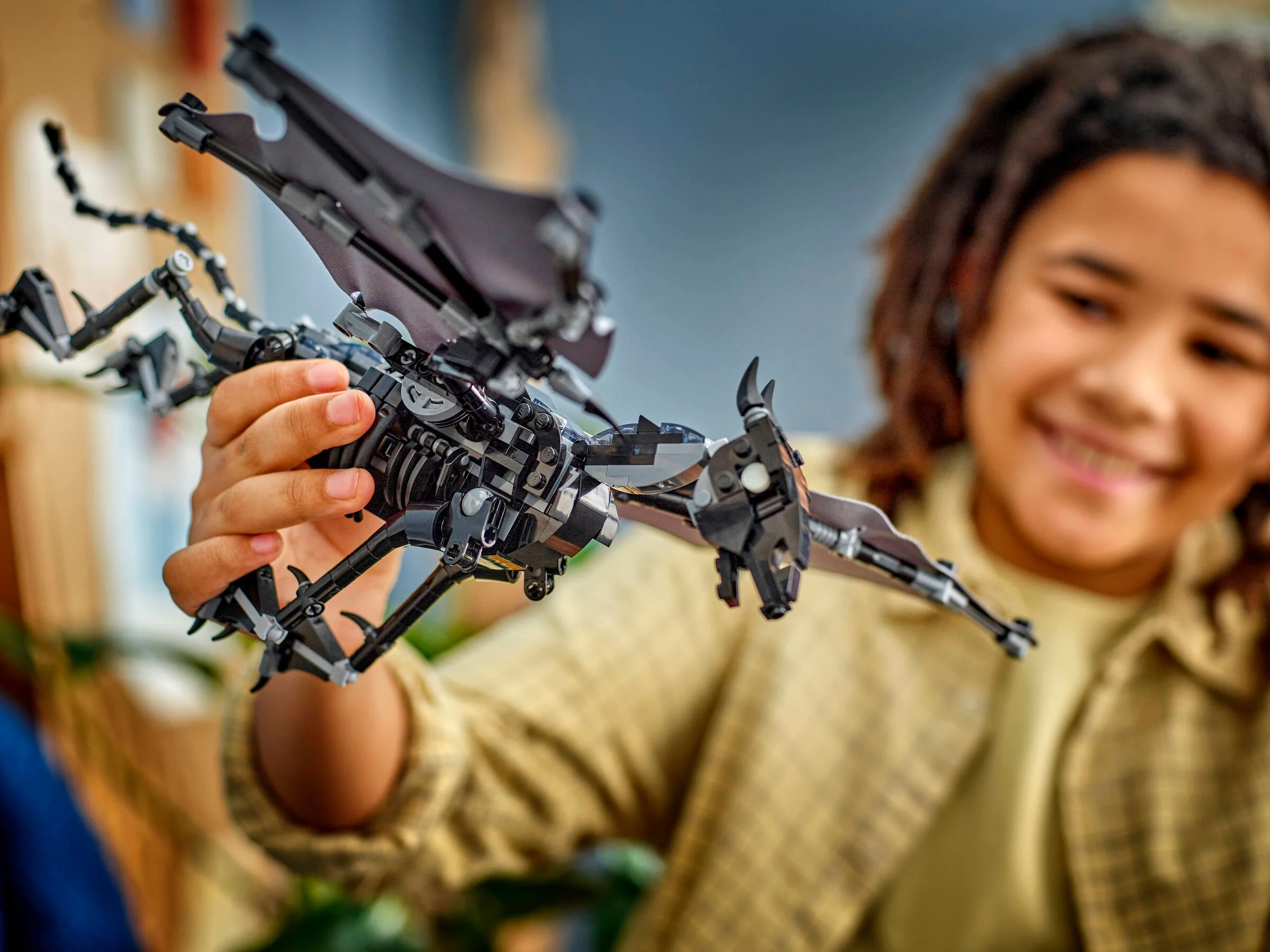Copil zâmbind ținând în mână un Thestral LEGO. Modelul este negru și are aripi mari.