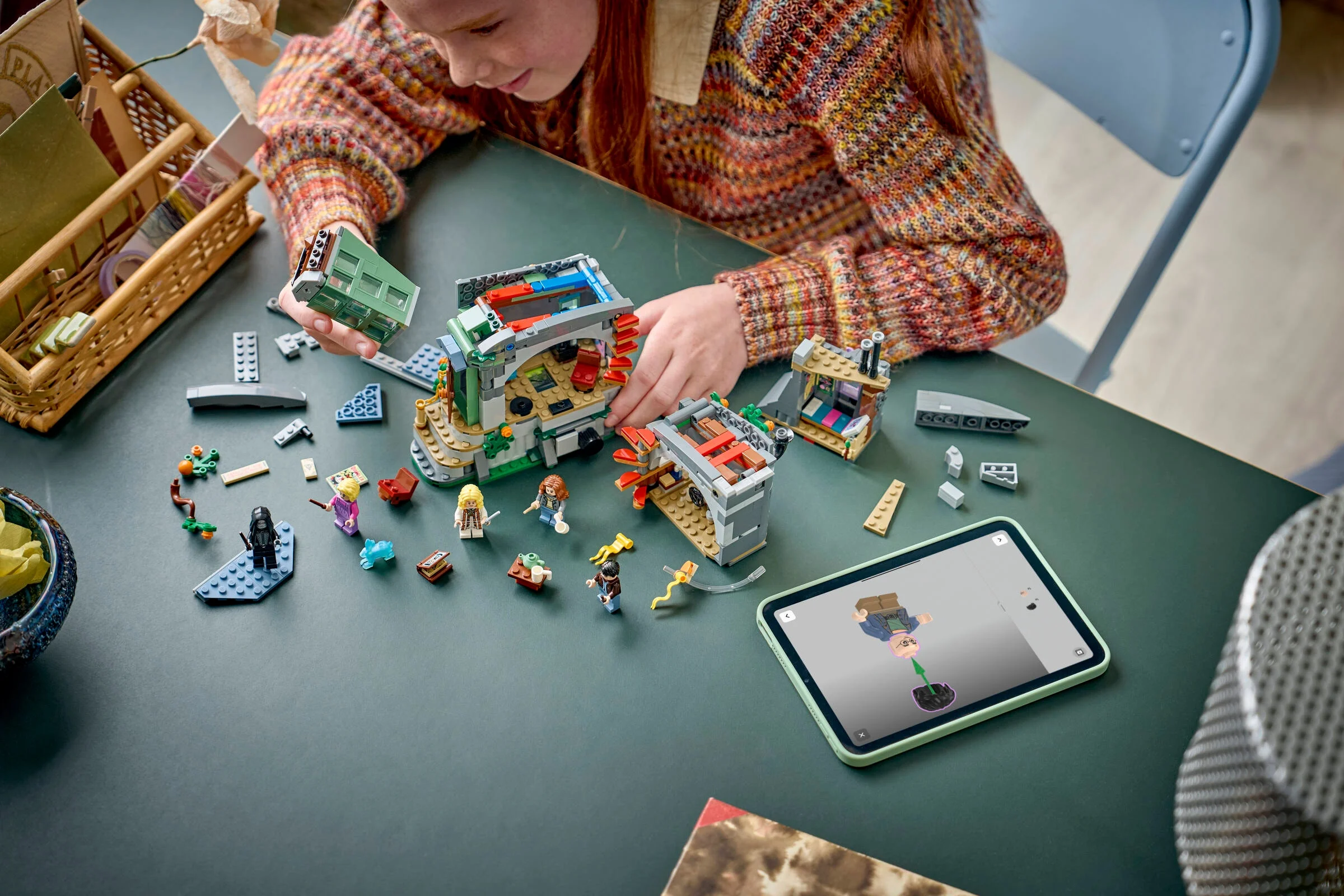 Fetiță construind casa Lunăi Lovegood, folosind instrucțiuni digitale pe tabletă. Detaliu model și minifigurine.