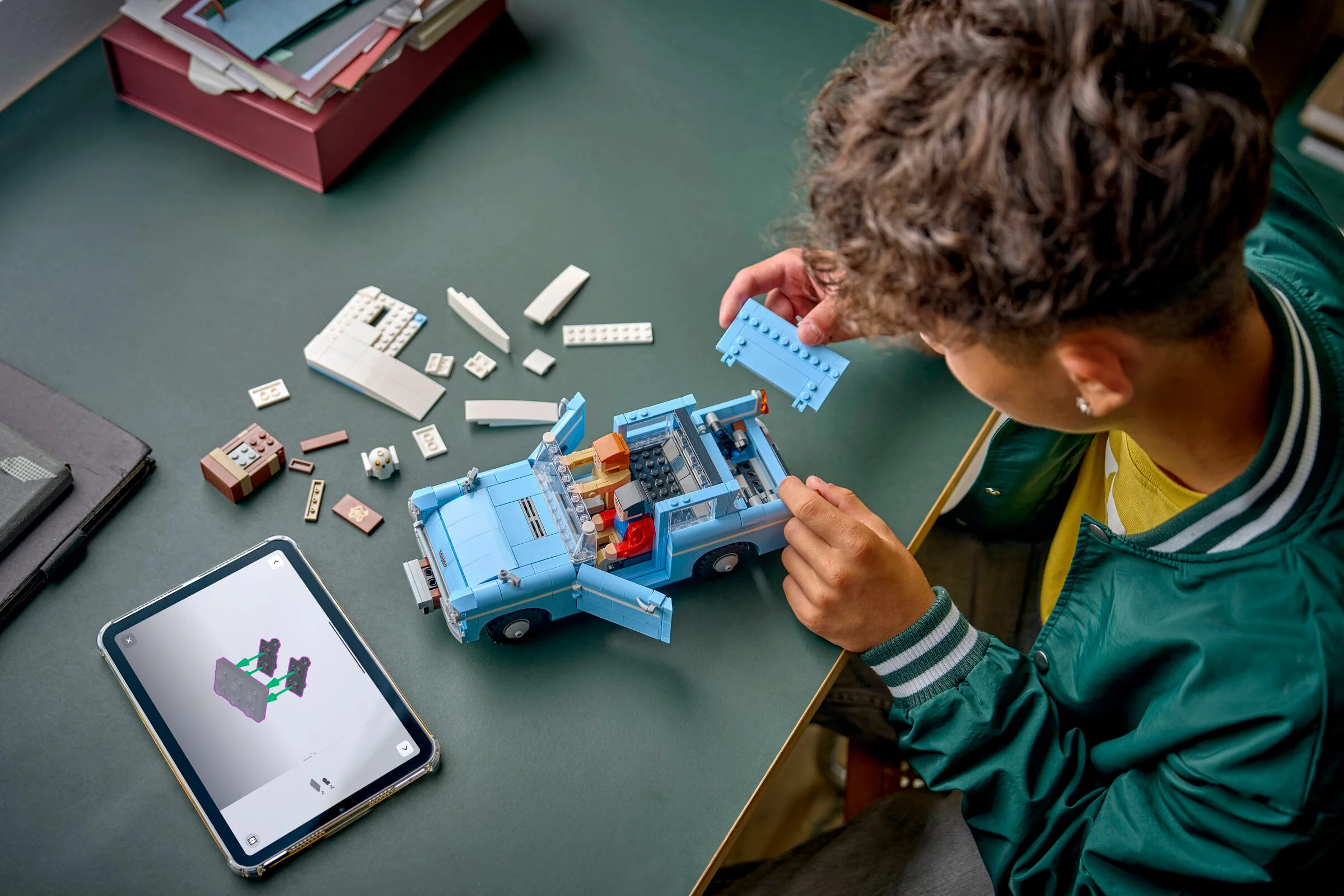Un copil construiește Ford Anglia fermecată LEGO, urmând instrucțiunile de pe tabletă.