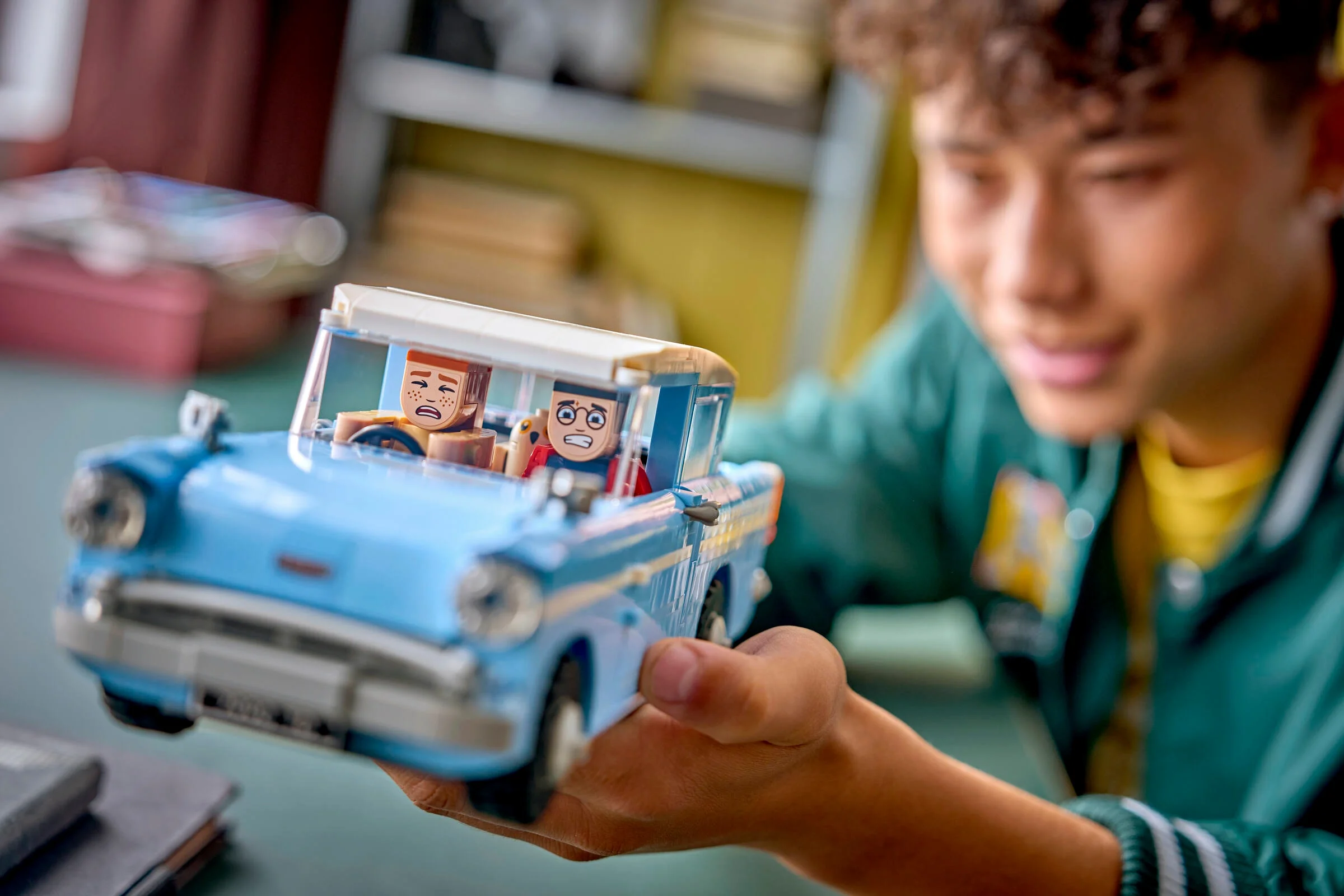 Un tânăr ține Ford Anglia zburătoare LEGO, cu Harry și Ron la bord, arătând aventura.