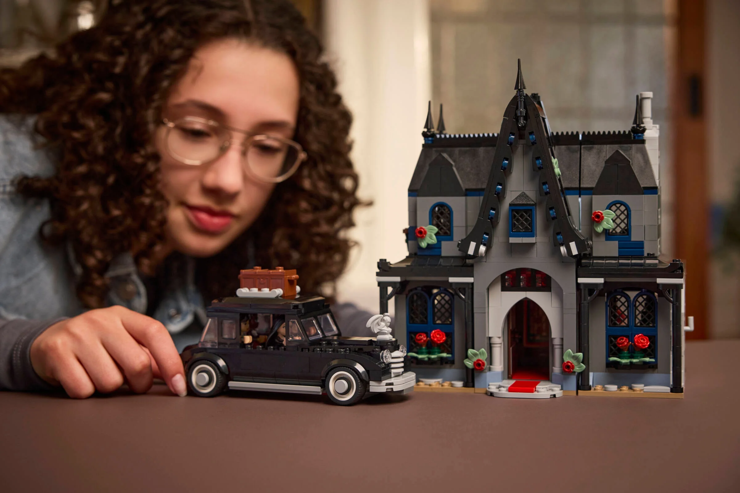 Modelul LEGO Casa Morticiei și mașina familiei Addams, prezentate de o tânără zâmbitoare.