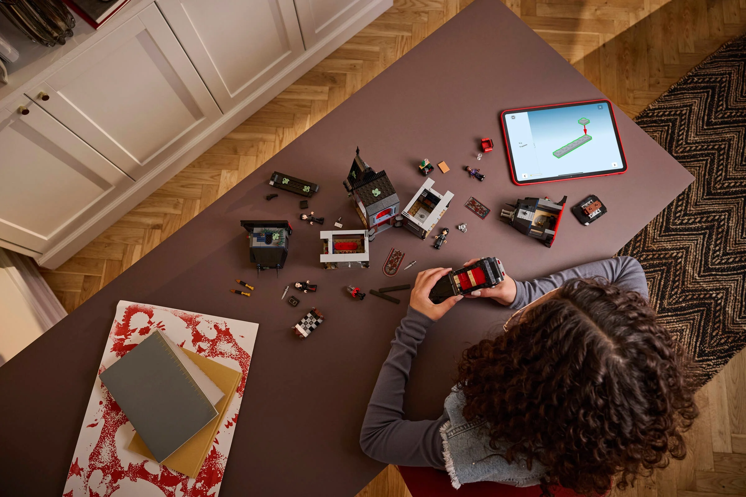 Imagine de sus arătând asamblarea parțială a Căsuței Morticiei, cu minifigurine și instrucțiuni digitale.