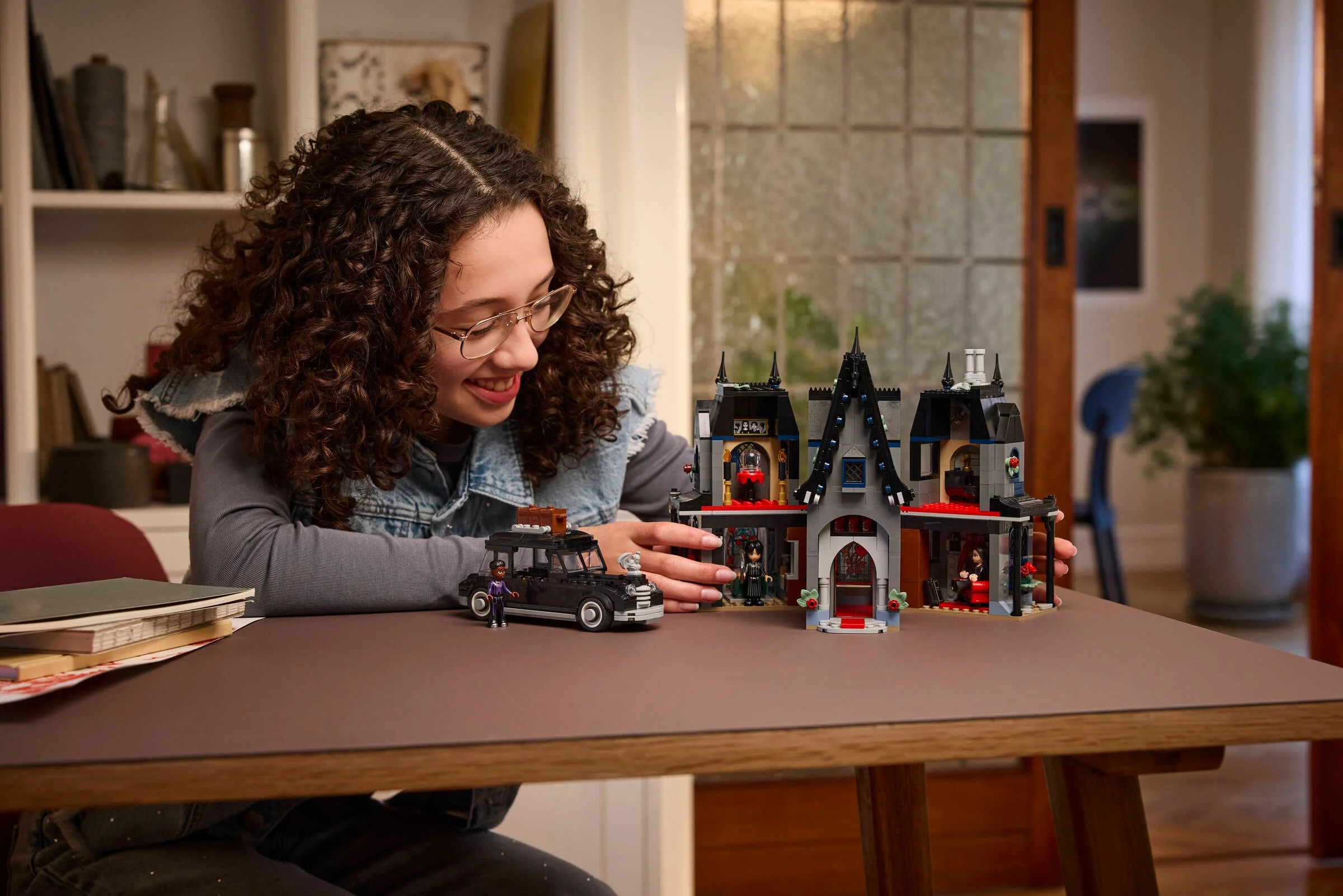 O tânără zâmbește admirând căsuța Morticiei, setul LEGO 76786, cu mașina și minifigurine.