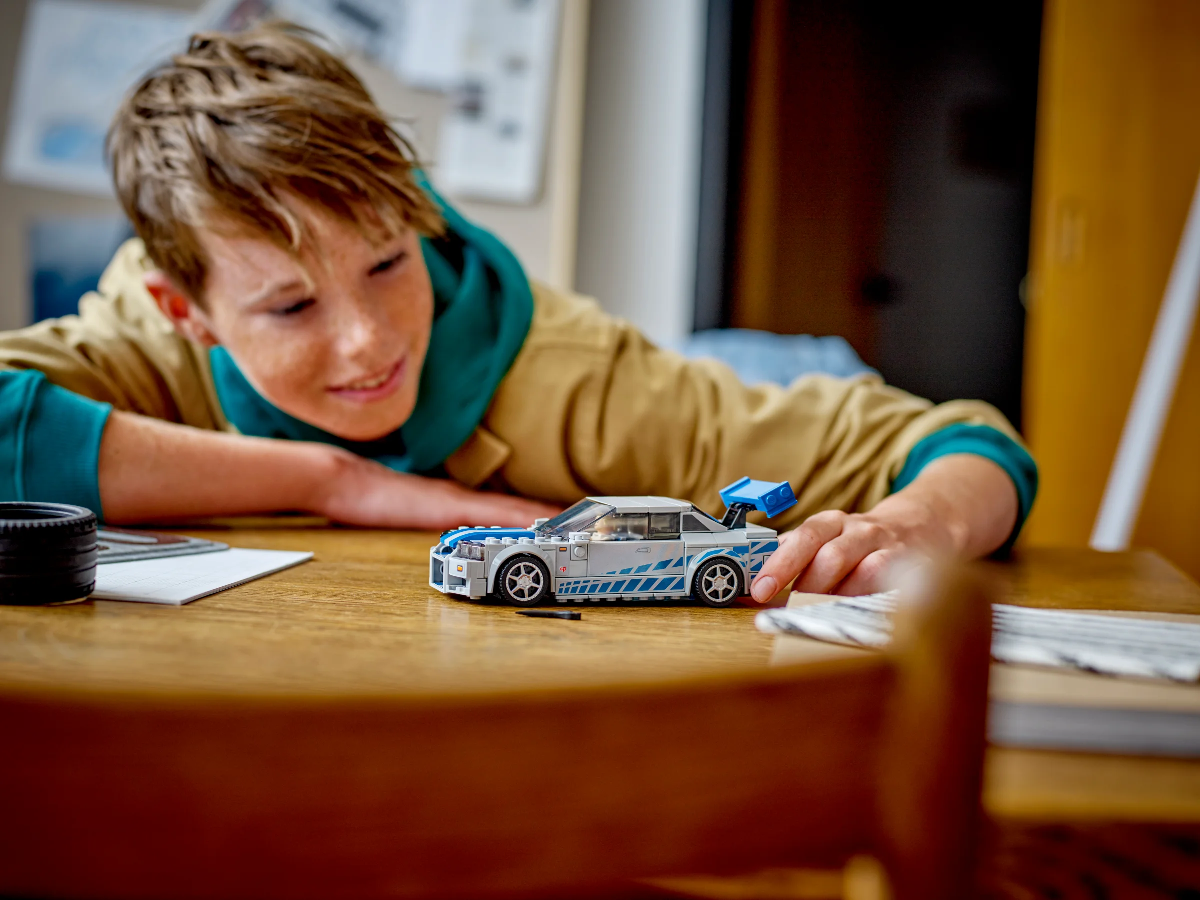 Copil zâmbind, joacă cu modelul LEGO Nissan Skyline GT-R (R34). Interacțiune acasă, atmosferă caldă.