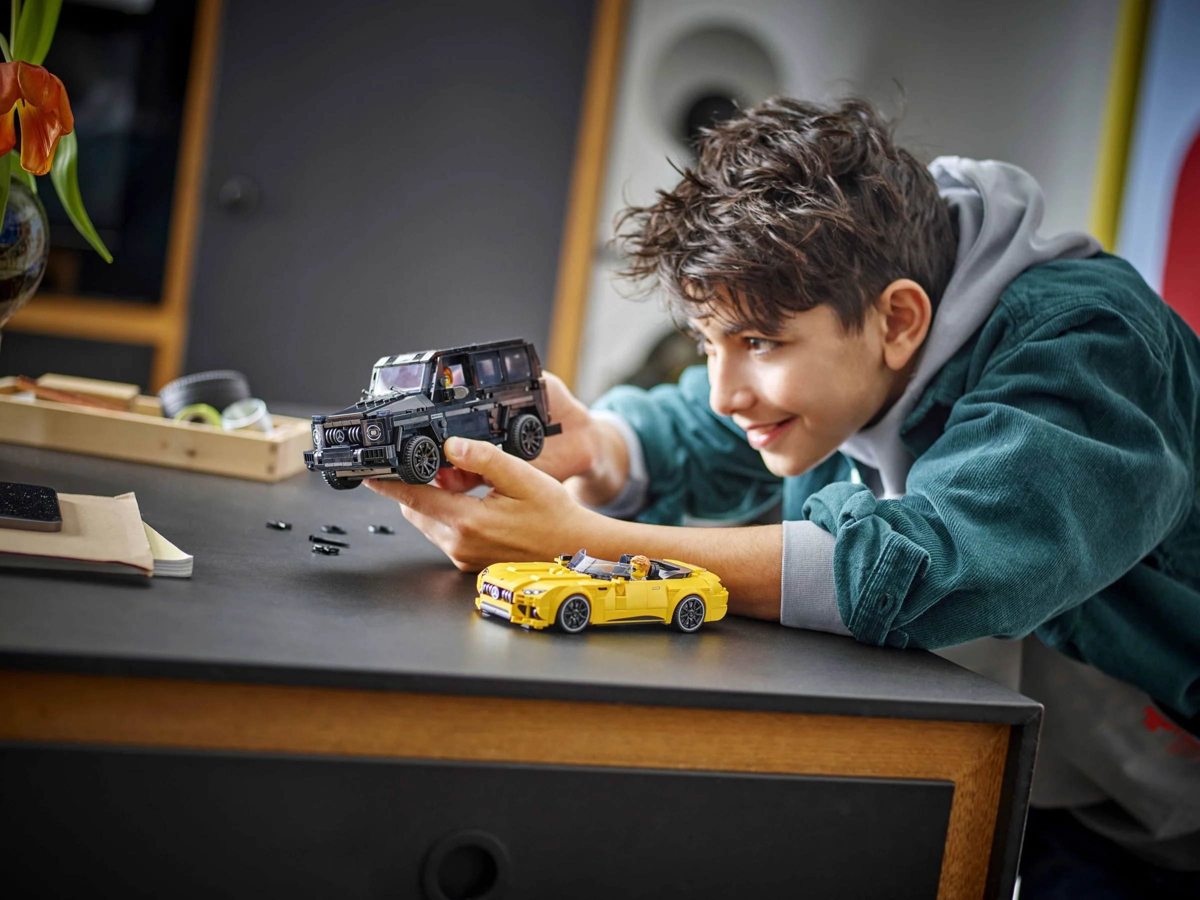 Un băiat se joacă cu modelele LEGO Mercedes-AMG G 63 și SL 63, zâmbind.