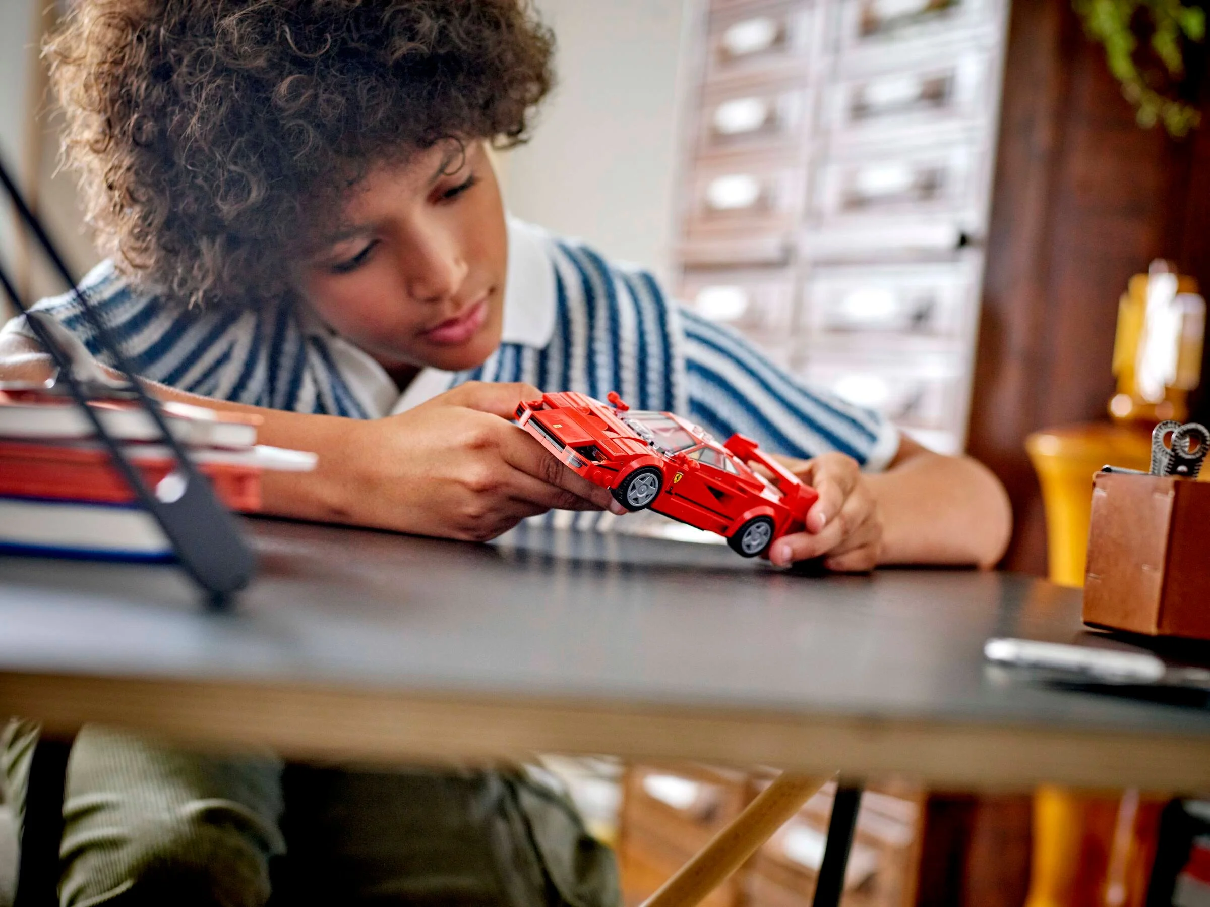 Băiat admirând o mașină Ferrari F40 LEGO roșie, o joacă cu atenție.