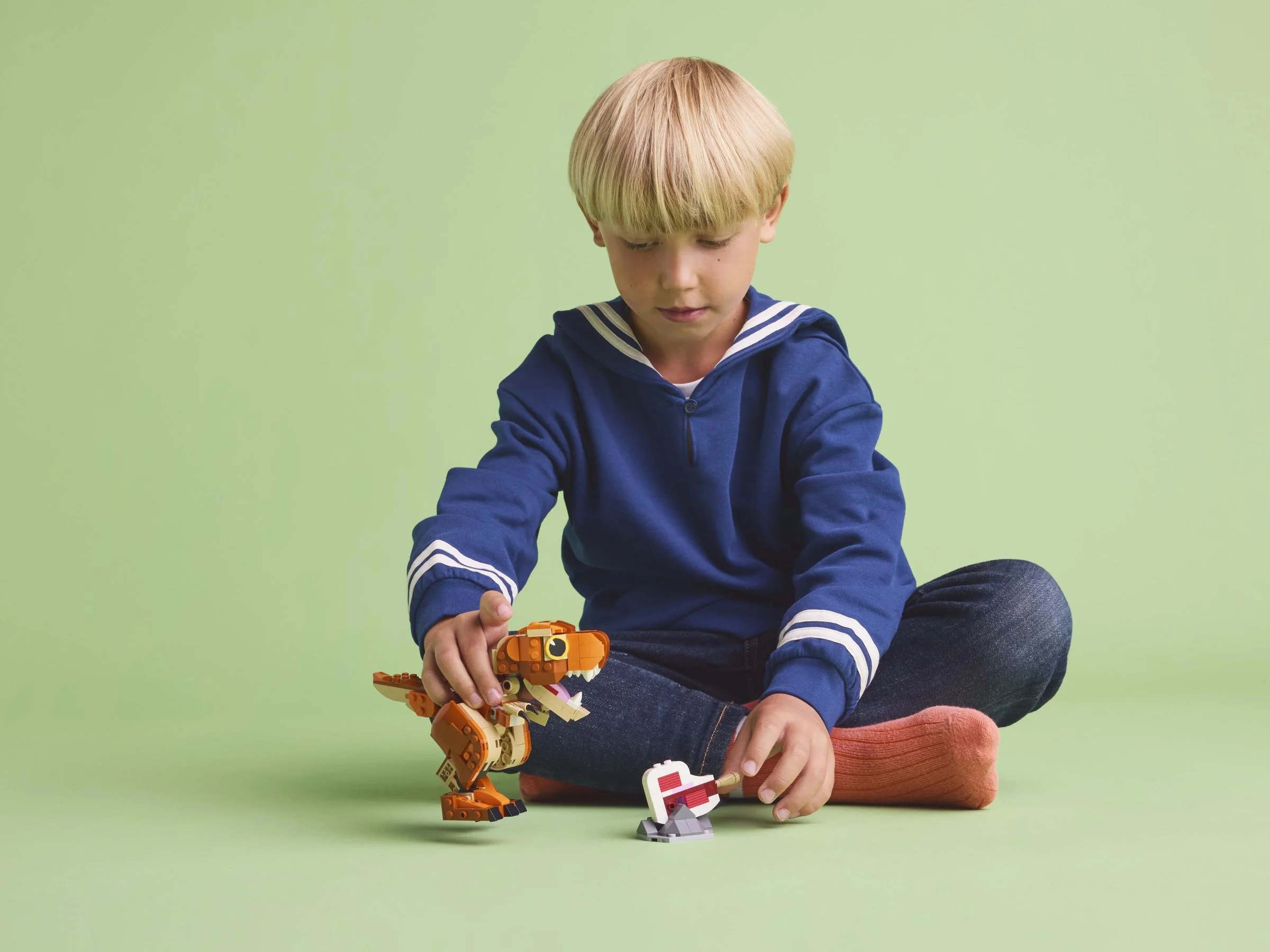 Un copil se joacă cu Little Eatie, un T. rex din LEGO, pe un fundal verde.