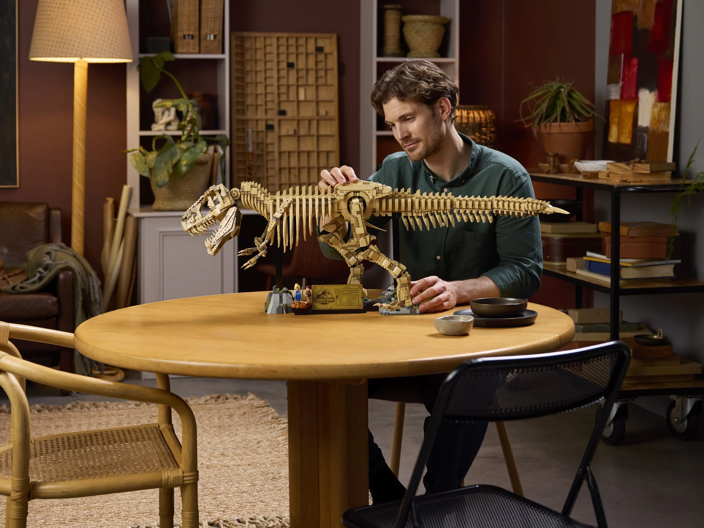 Un bărbat examinează scheletul T-Rex LEGO, așezat pe o masă rotundă. Detaliu impresionant al modelului.