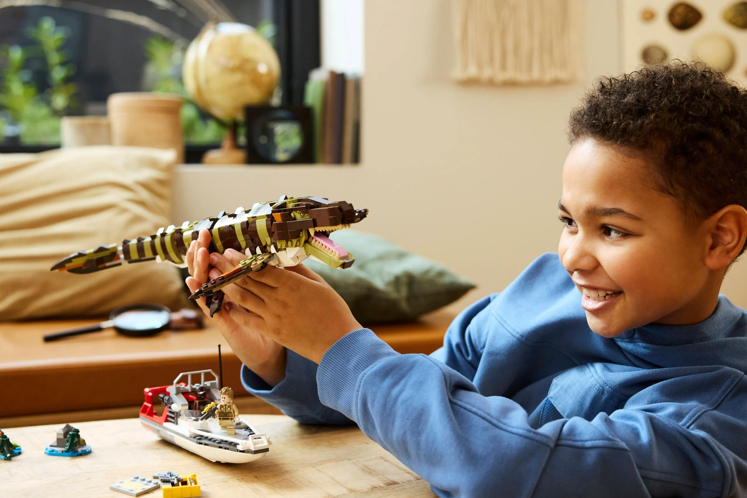 Un băiat zâmbește ținând Mosasaurul construit din cărămizi LEGO.