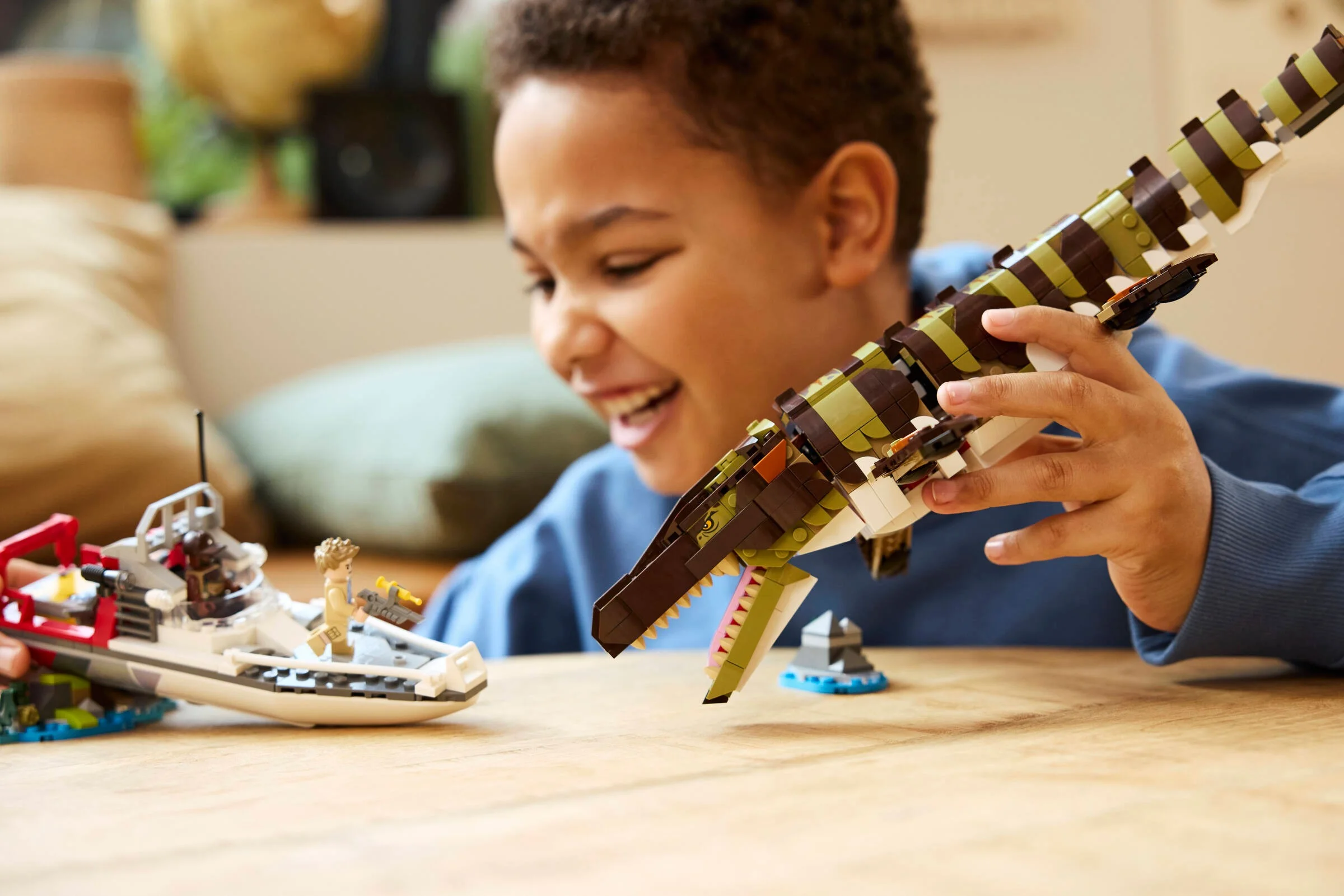 Copil zâmbind, jucându-se cu setul LEGO Mosasaurus. Setul include o barcă și un Mosasaur construit din cărămizi.