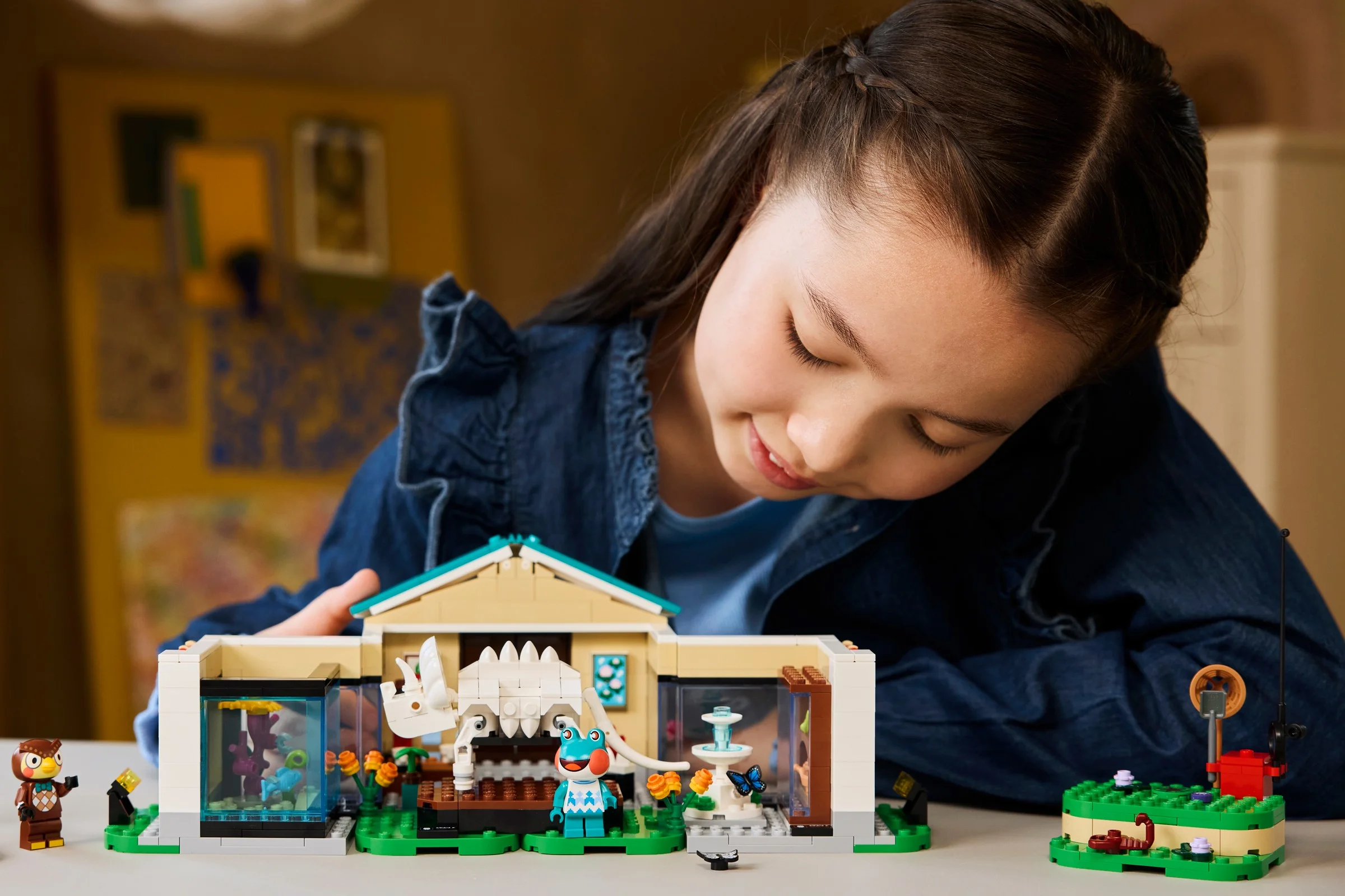 O fată zâmbește în timp ce se uită la setul LEGO Muzeul lui Blathers, arătând construcția și minifigurinele.