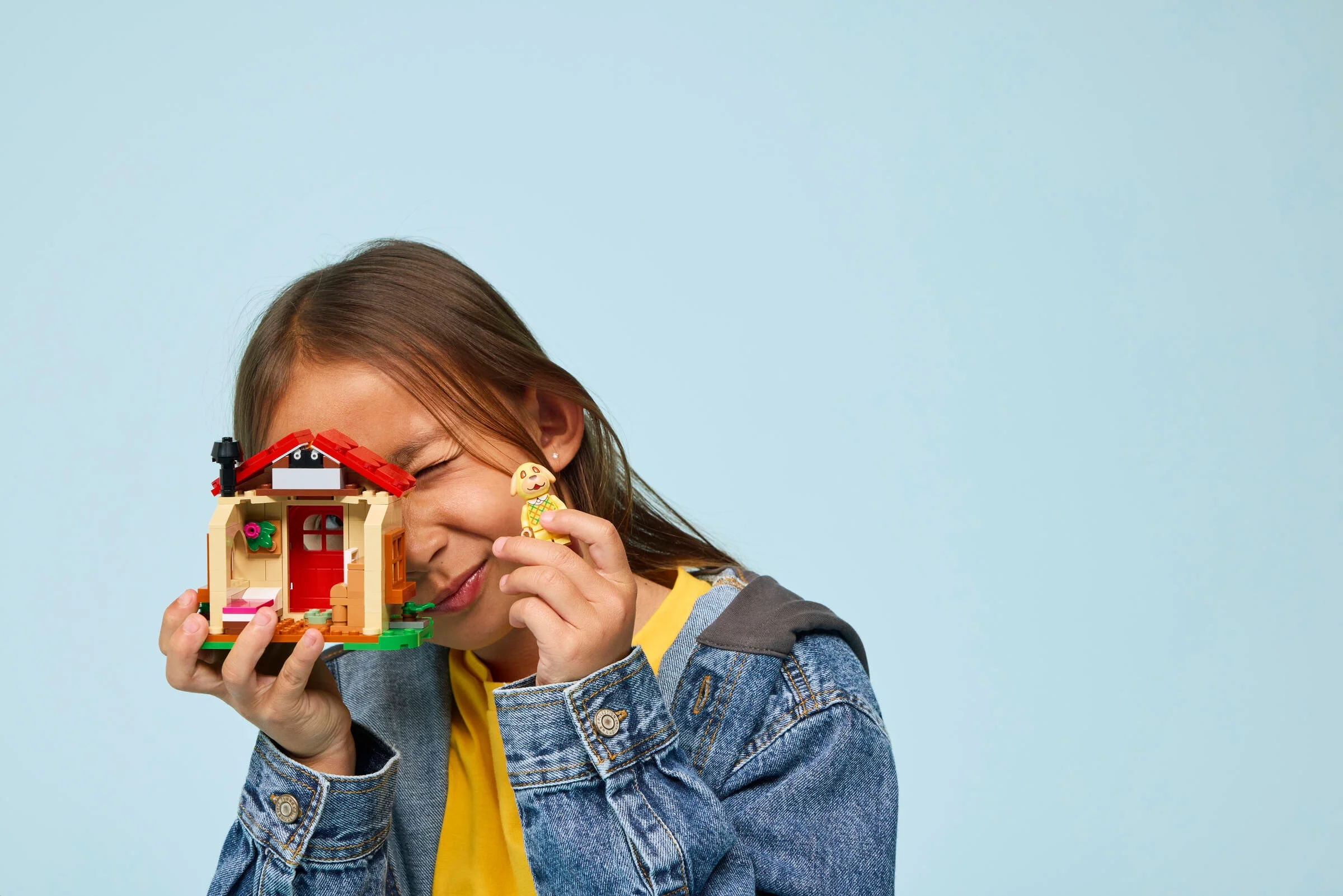 Fetiță ținând căsuța LEGO Goldie, zâmbind cu ochii închiși. Set simpatic Animal Crossing.