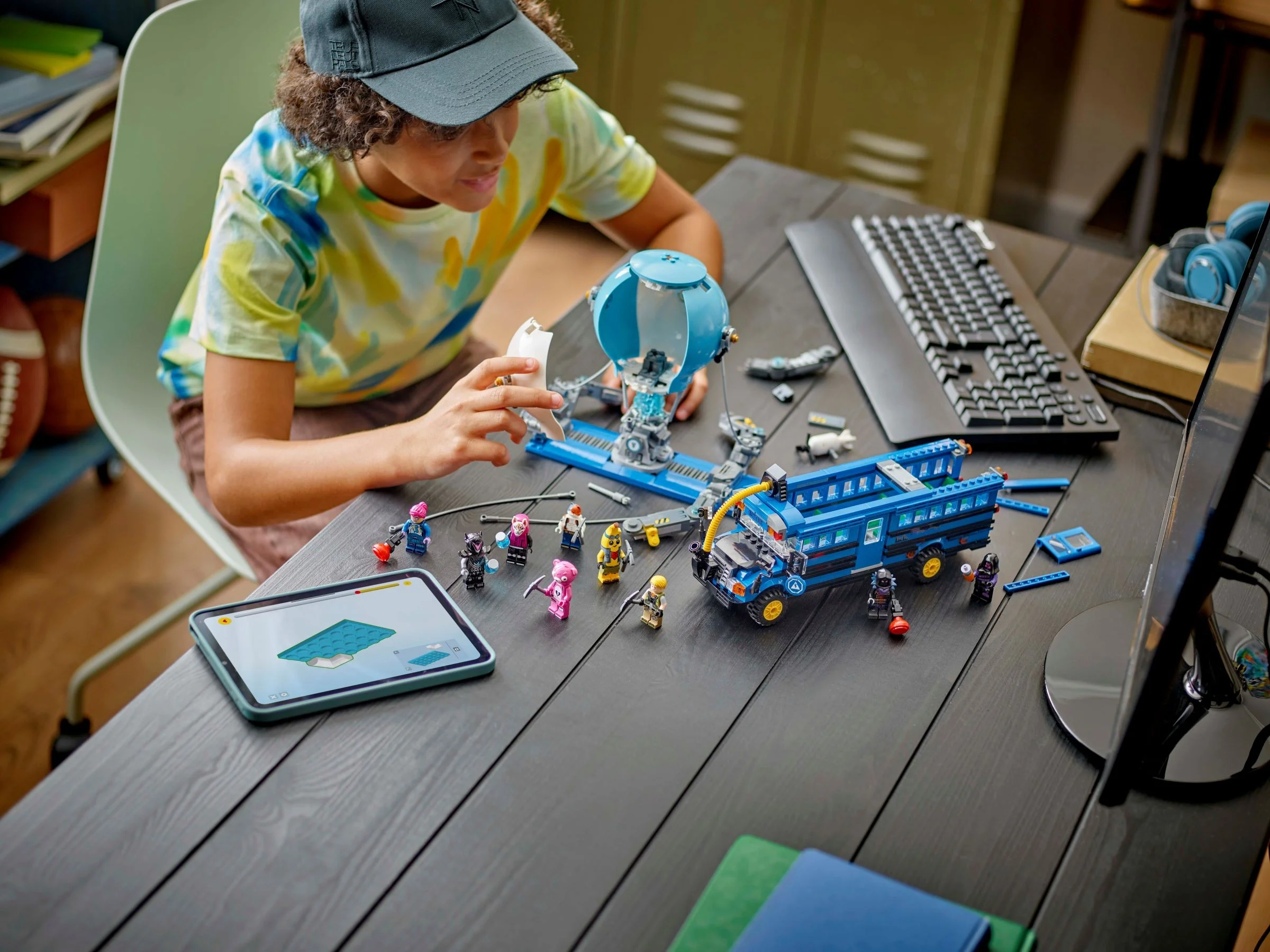 Copil construind setul Fortnite cu instrucțiuni pe tabletă. Autobuzul și minifigurinele sunt vizibile.