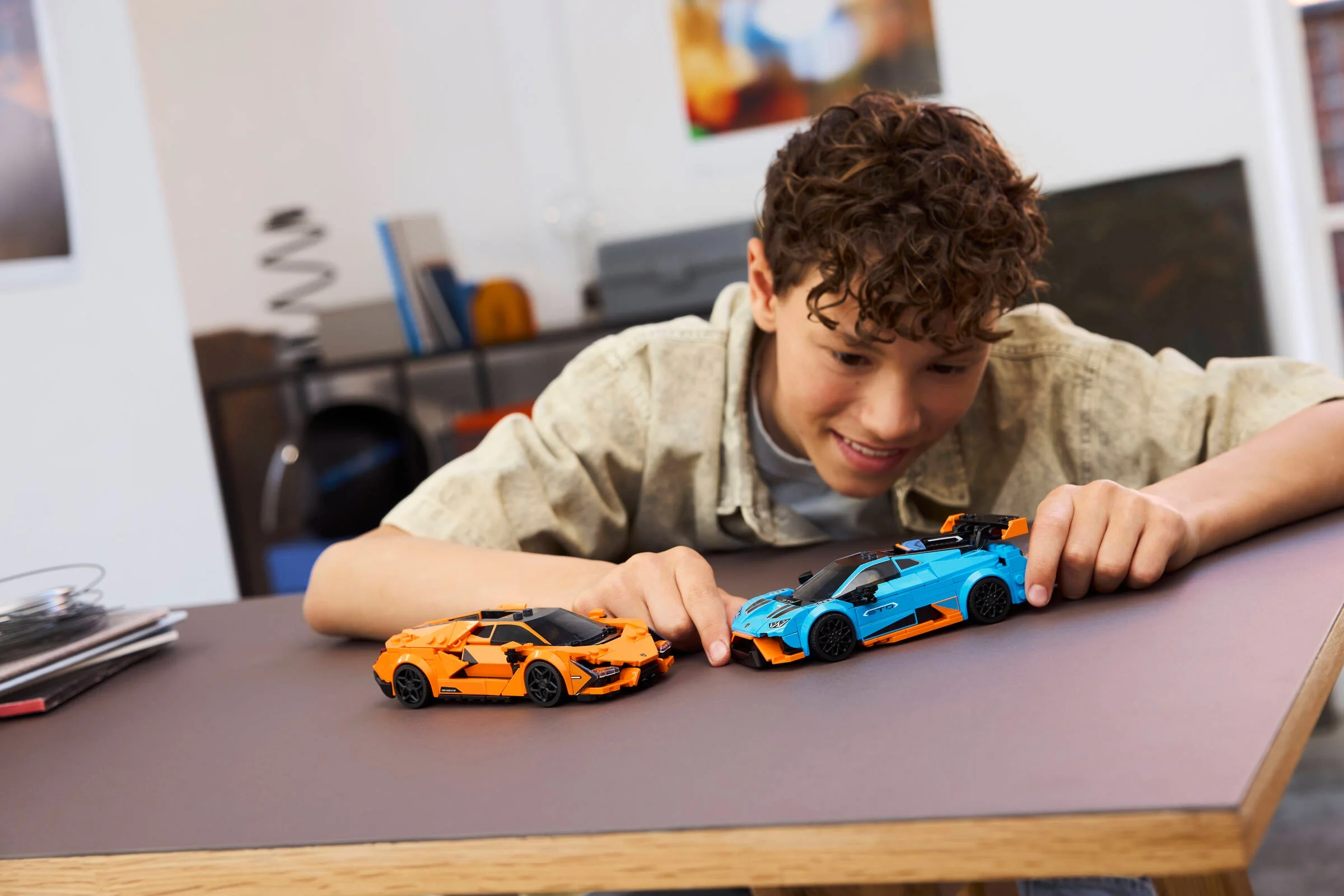 Băiat se joacă cu modelele LEGO Lamborghini Revuelto și Huracán STO pe o masă. 