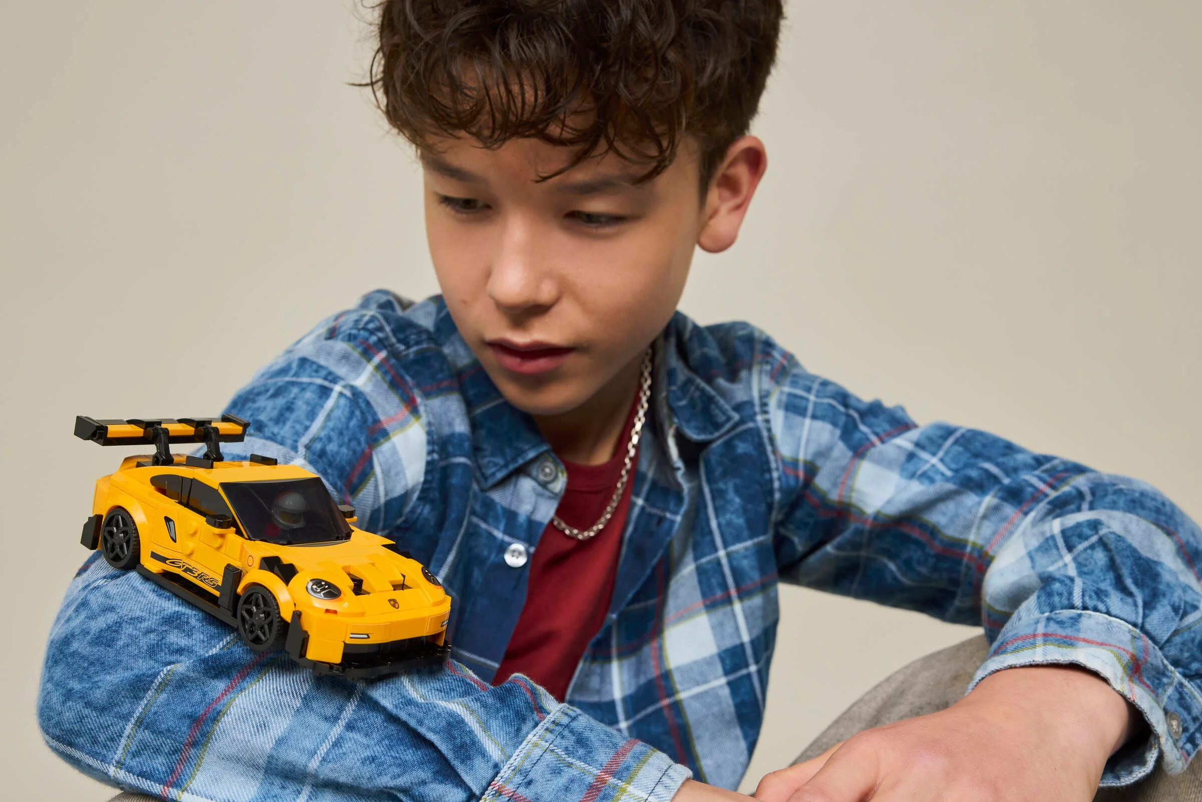 Un băiat admiră o mașină Porsche 911 GT3 RS galbenă, construită din LEGO Speed Champions.